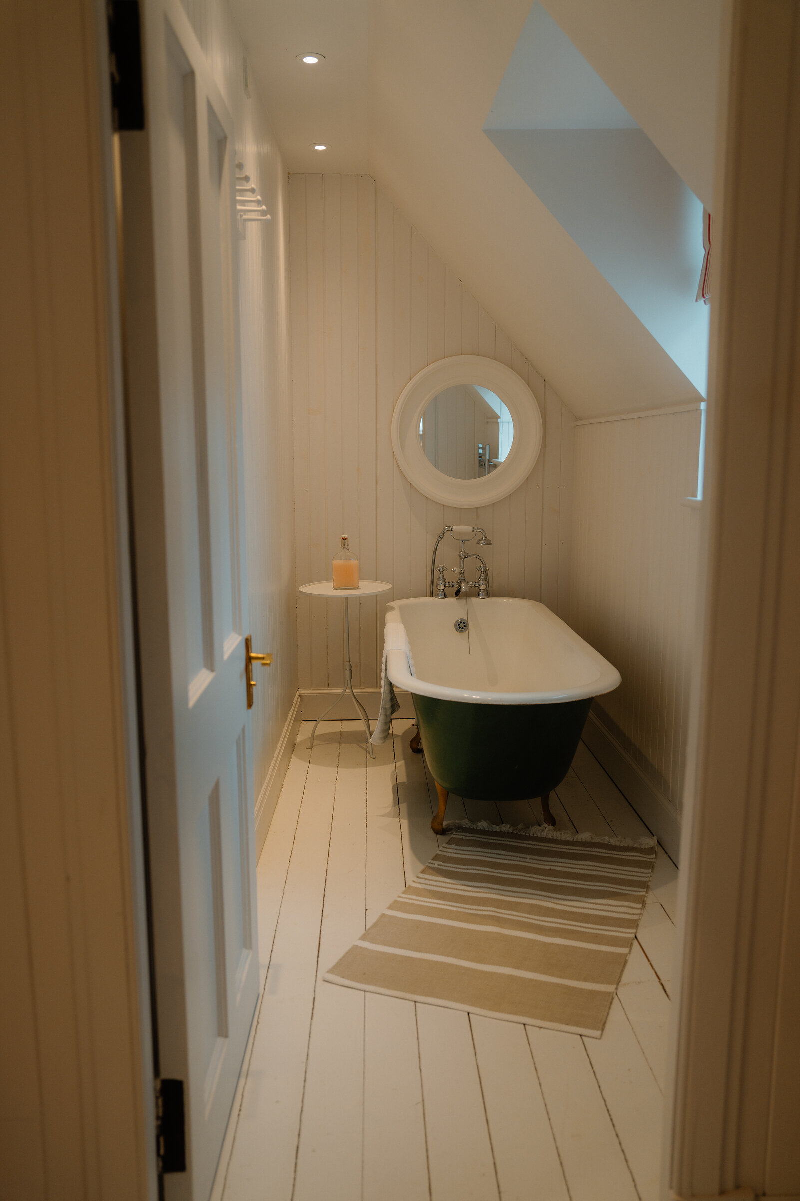 A green clawfoot bathtub sits beneath a round mirror in a sloped-ceiling bathroom at Coruisk House.