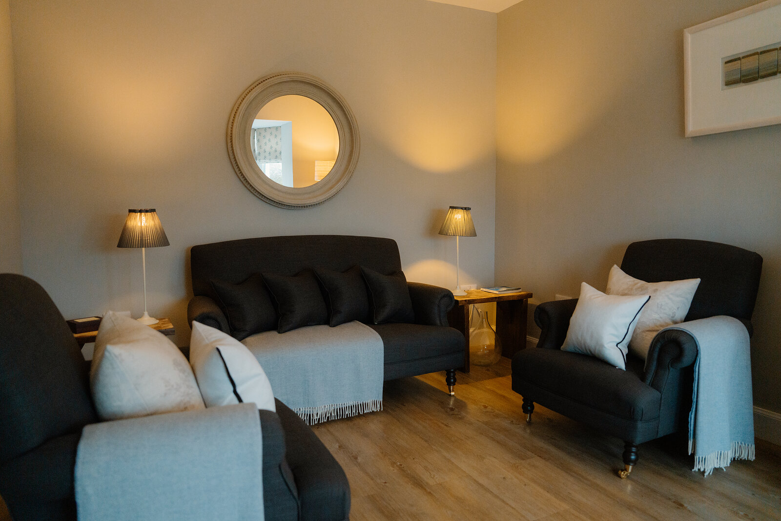 Dark green sofas and an armchair are arranged beneath a round mirror in a lounge at Coruisk House.