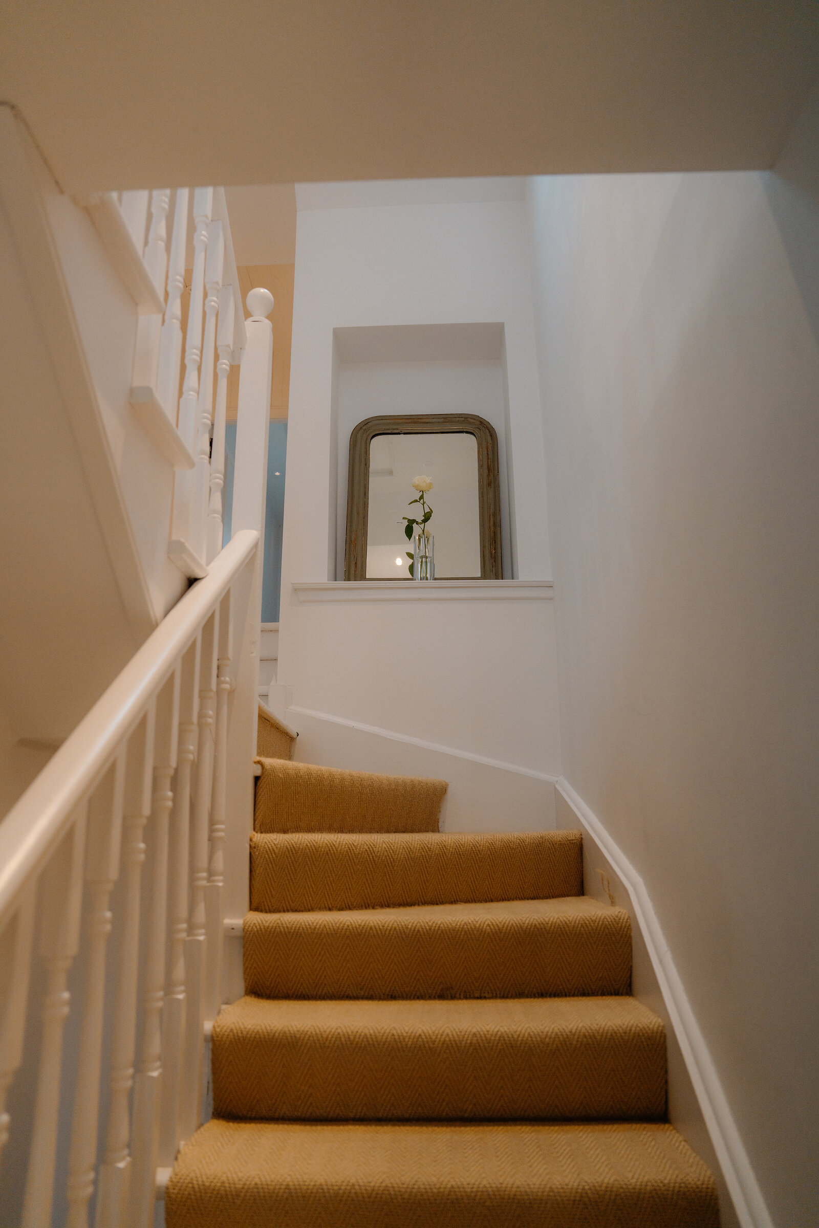 A carpeted staircase at Coruisk House climbs past a landing mirror holding a single rose.