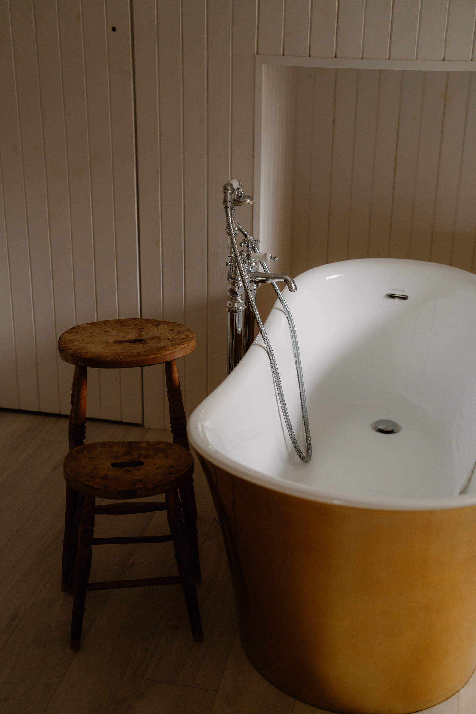 A mustard-coloured freestanding bathtub with wall-mounted taps stands beside a wooden stool in a panelled bathroom at Coruisk House.