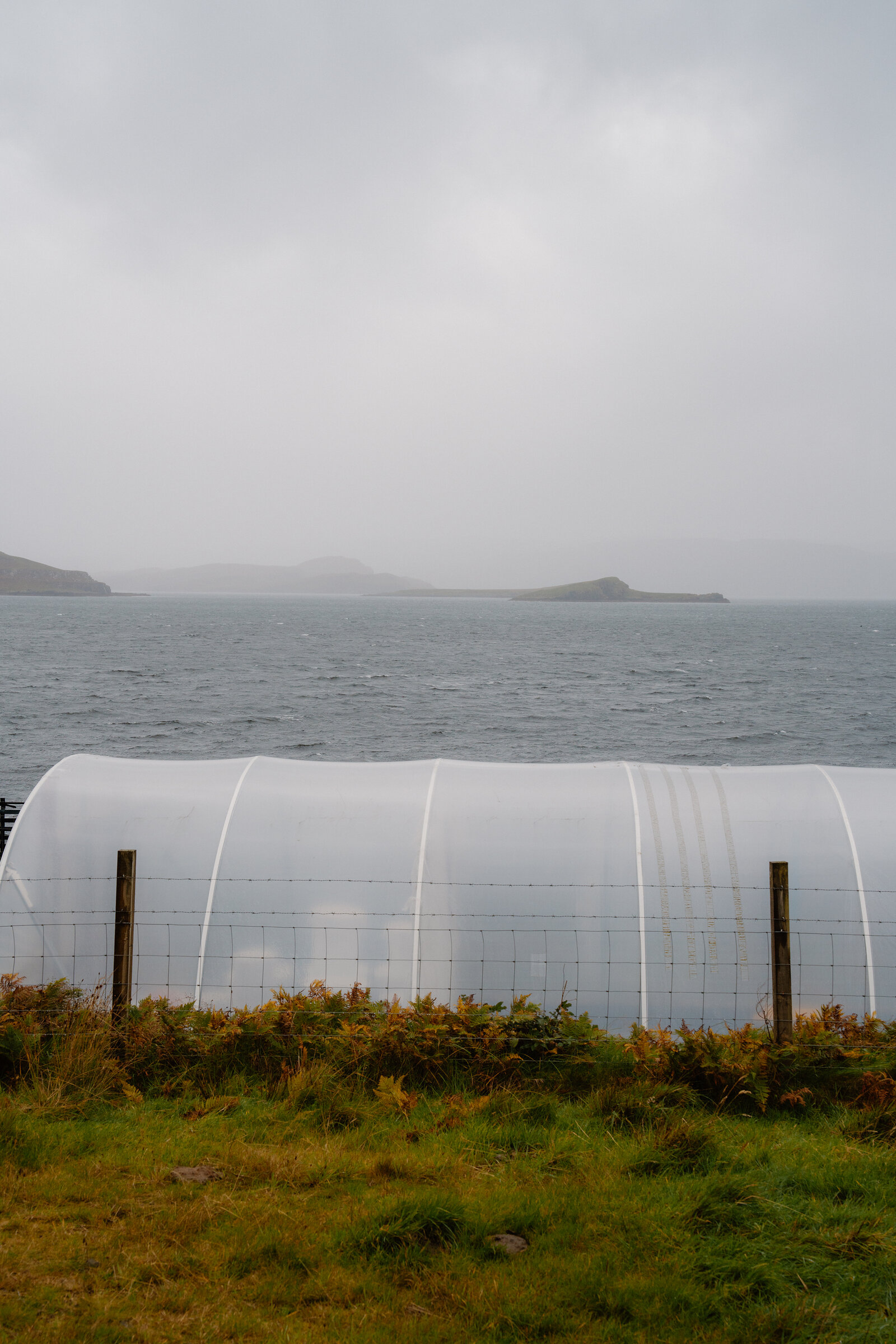 A polytunnel for evaporating seawater stands beside a misty sea loch dotted with small islands at Isle of Skye Sea Salt Company.