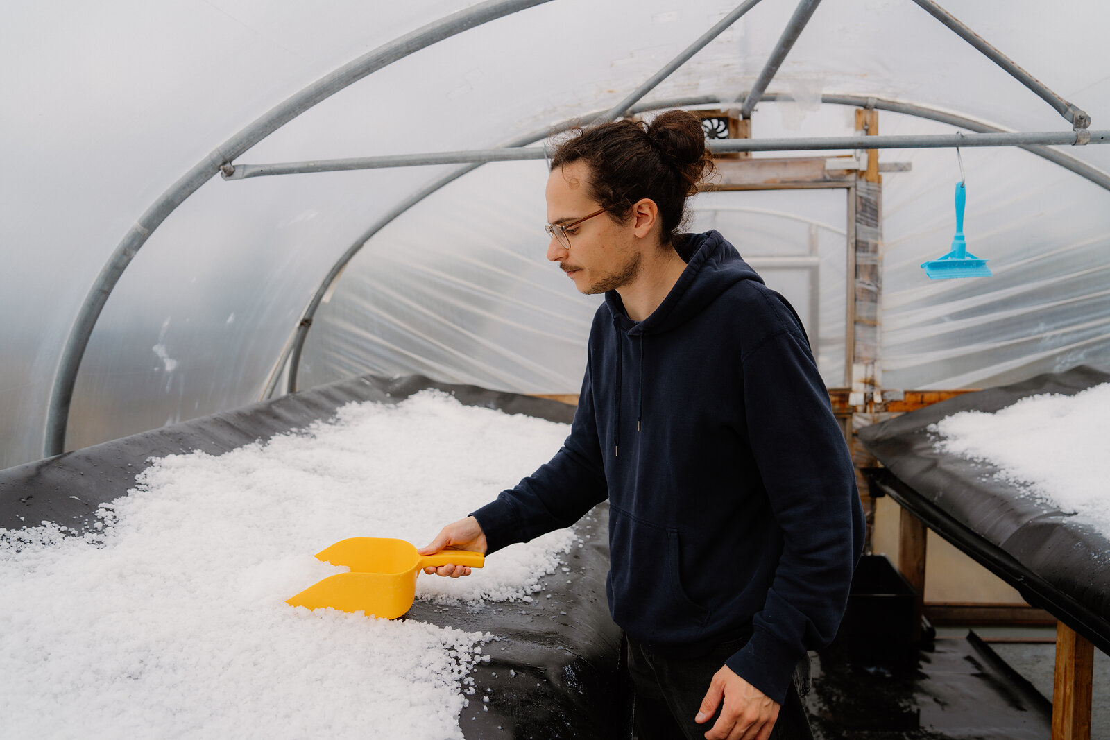 A man rakes salt crystals with a yellow scoop inside a seawater evaporation polytunnel at Isle of Skye Sea Salt Company.