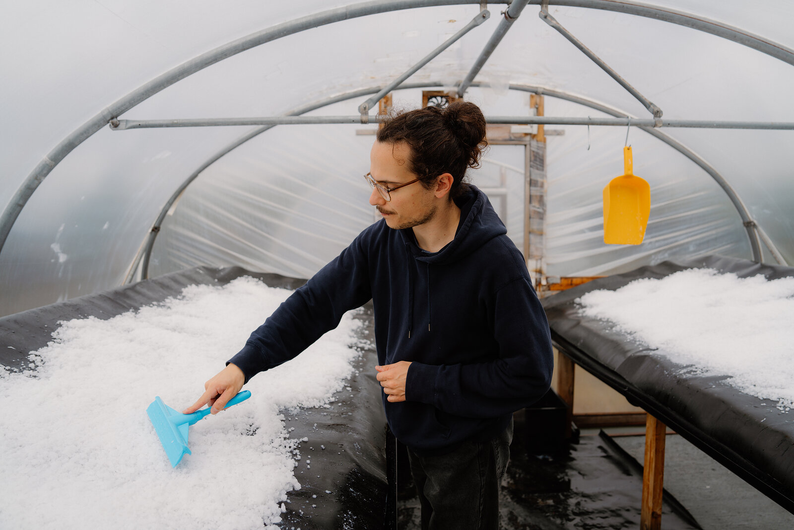 A man gathers salt crystals with a blue squeegee inside a seawater evaporation polytunnel at Isle of Skye Sea Salt Company.