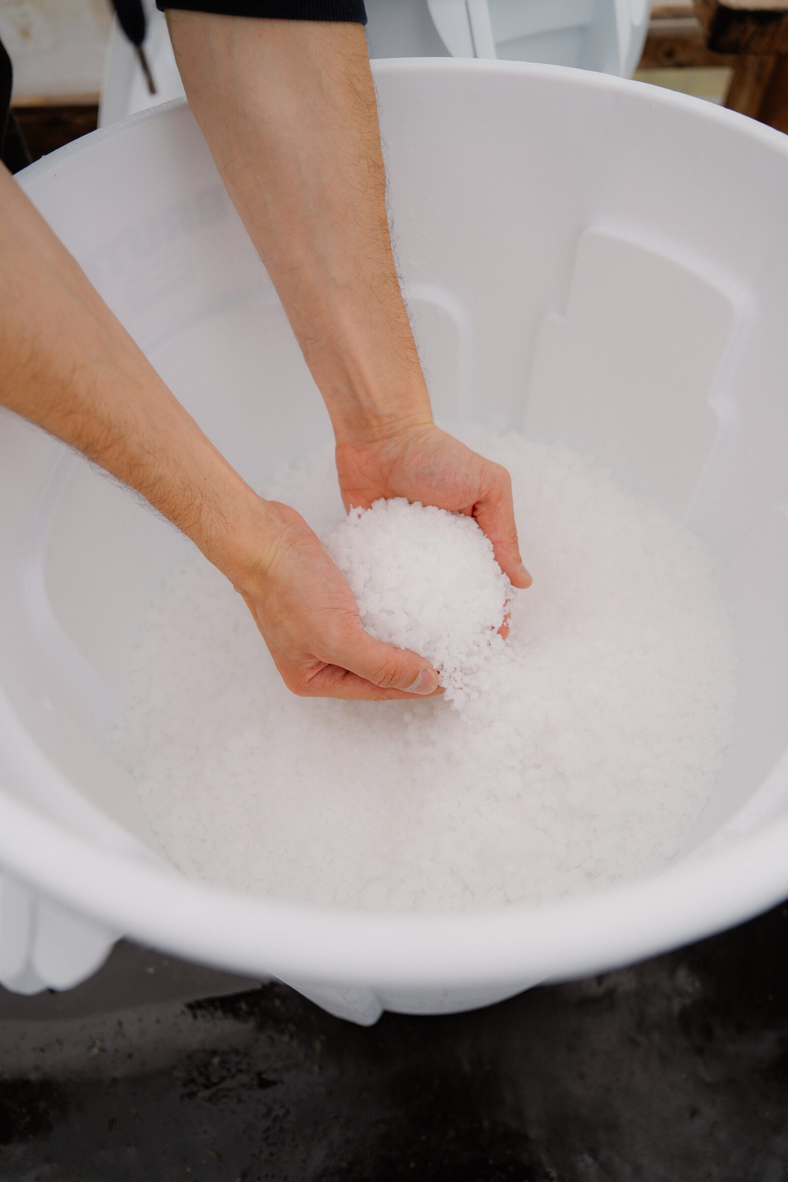 Two hands scoop sea salt crystals from a white bucket at Isle of Skye Sea Salt Company.