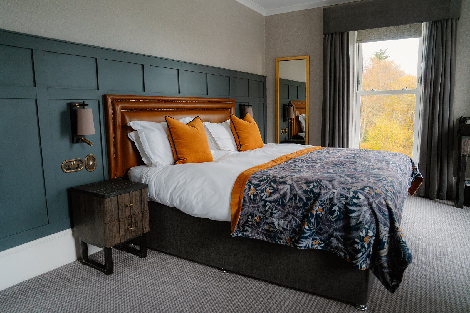 A tan leather headboard with orange cushions stands against a teal-panelled wall in a Skeabost bedroom, part of the Sonas Collection.