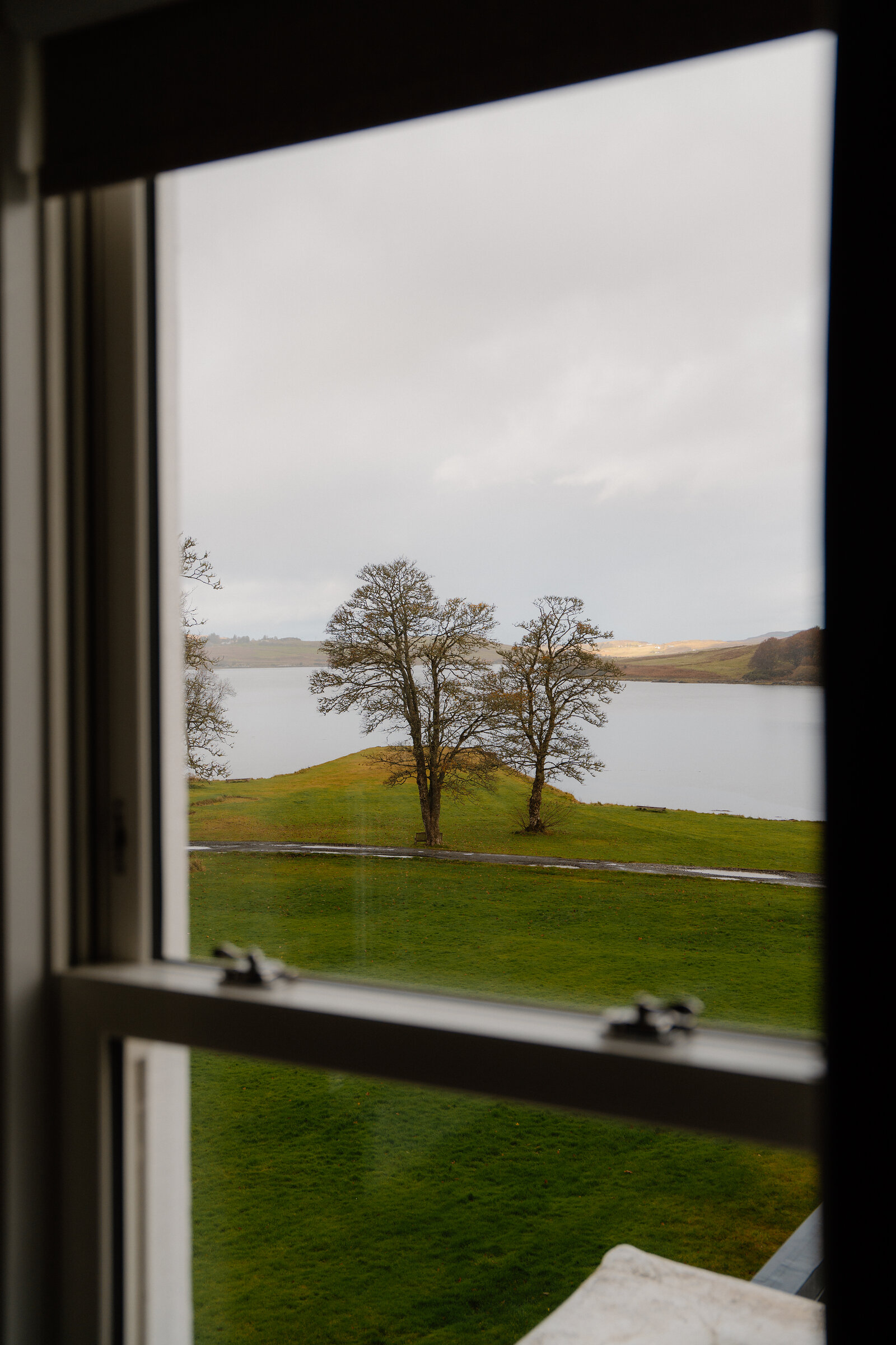 A window at Skeabost frames a view through bare trees to a loch beyond.