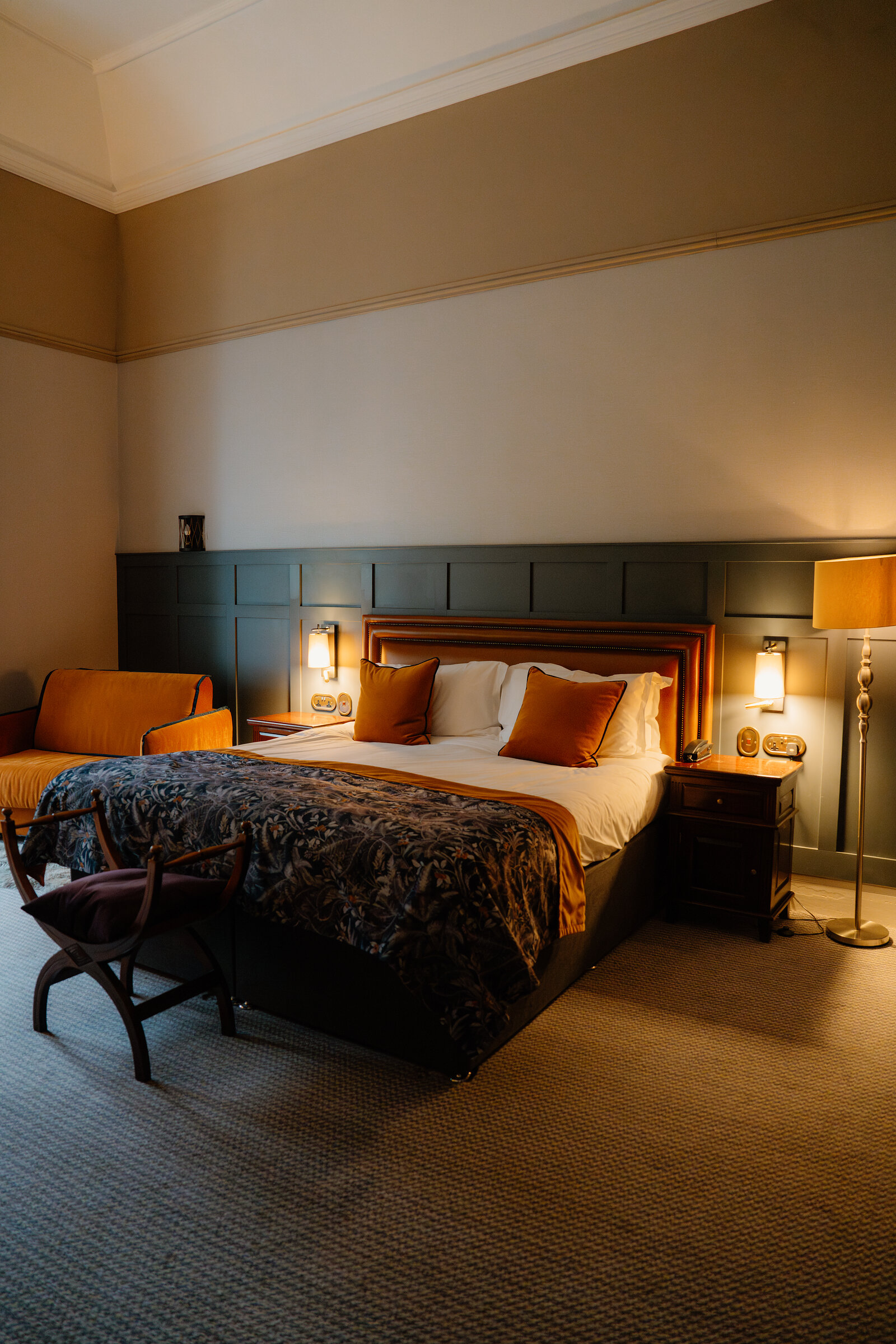 A bed with orange cushions sits against a dark green panelled wall beside an orange armchair in a Skeabost bedroom, part of the Sonas Collection.