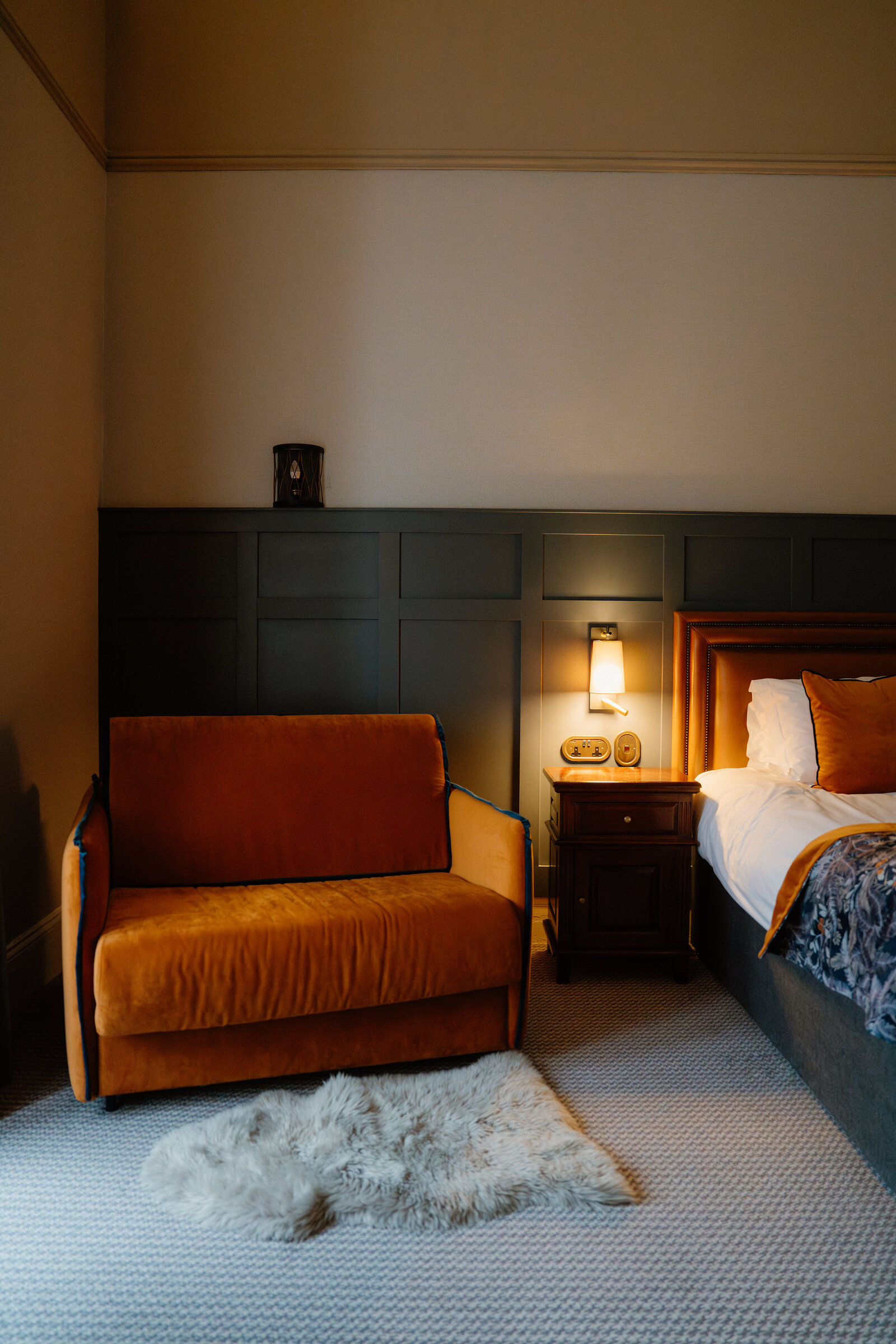 An orange velvet armchair and a sheepskin rug sit in a dark green panelled Skeabost bedroom, part of the Sonas Collection.