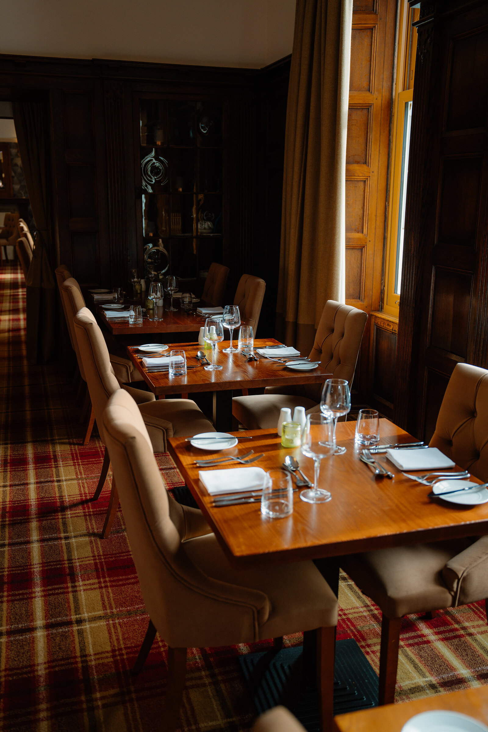 Wood-panelled walls and a glass cabinet line a Skeabost dining room set with tables beside a window.