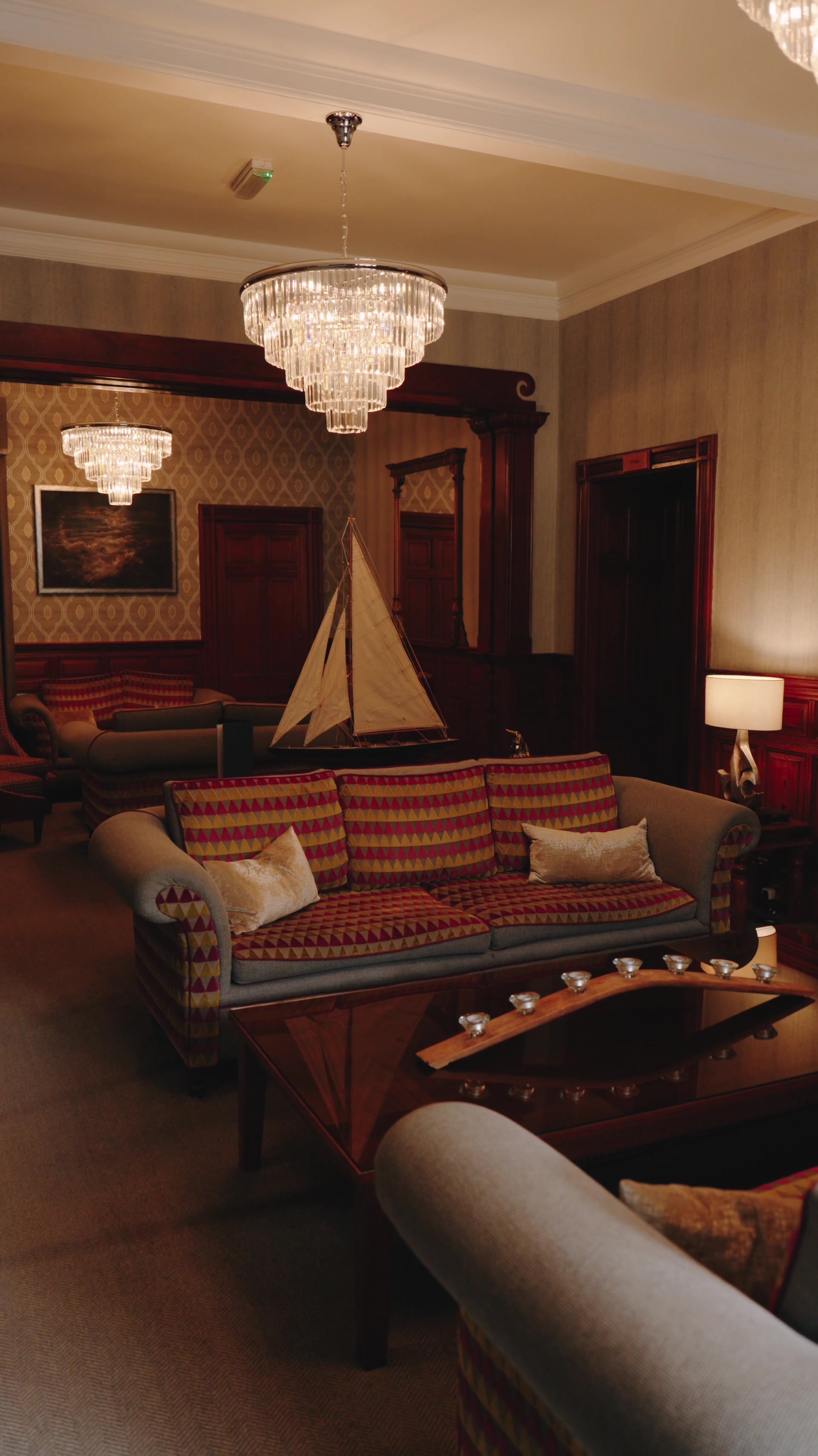 Crystal chandeliers hang above patterned sofas and a model sailing yacht in an opulent wood-panelled lounge.