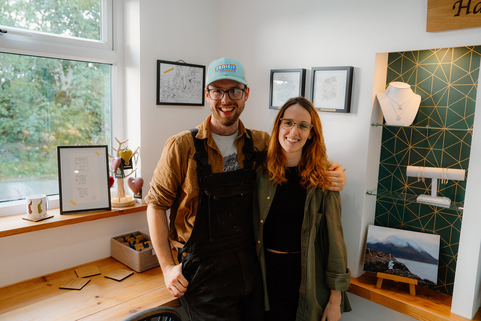 A man holds a black and white dog beside a smiling woman in a room hung with framed prints and jewellery display cases at The Exchange.