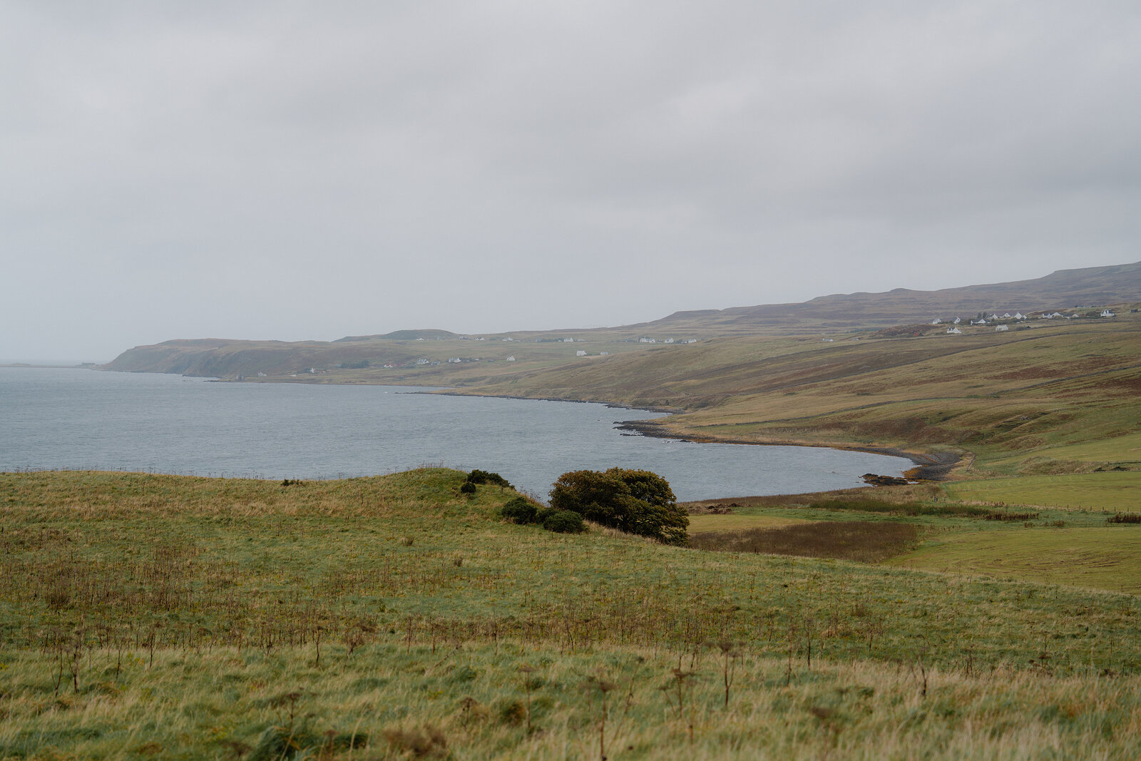 A curving bay bordered by hills and a scattering of houses under a heavy sky
