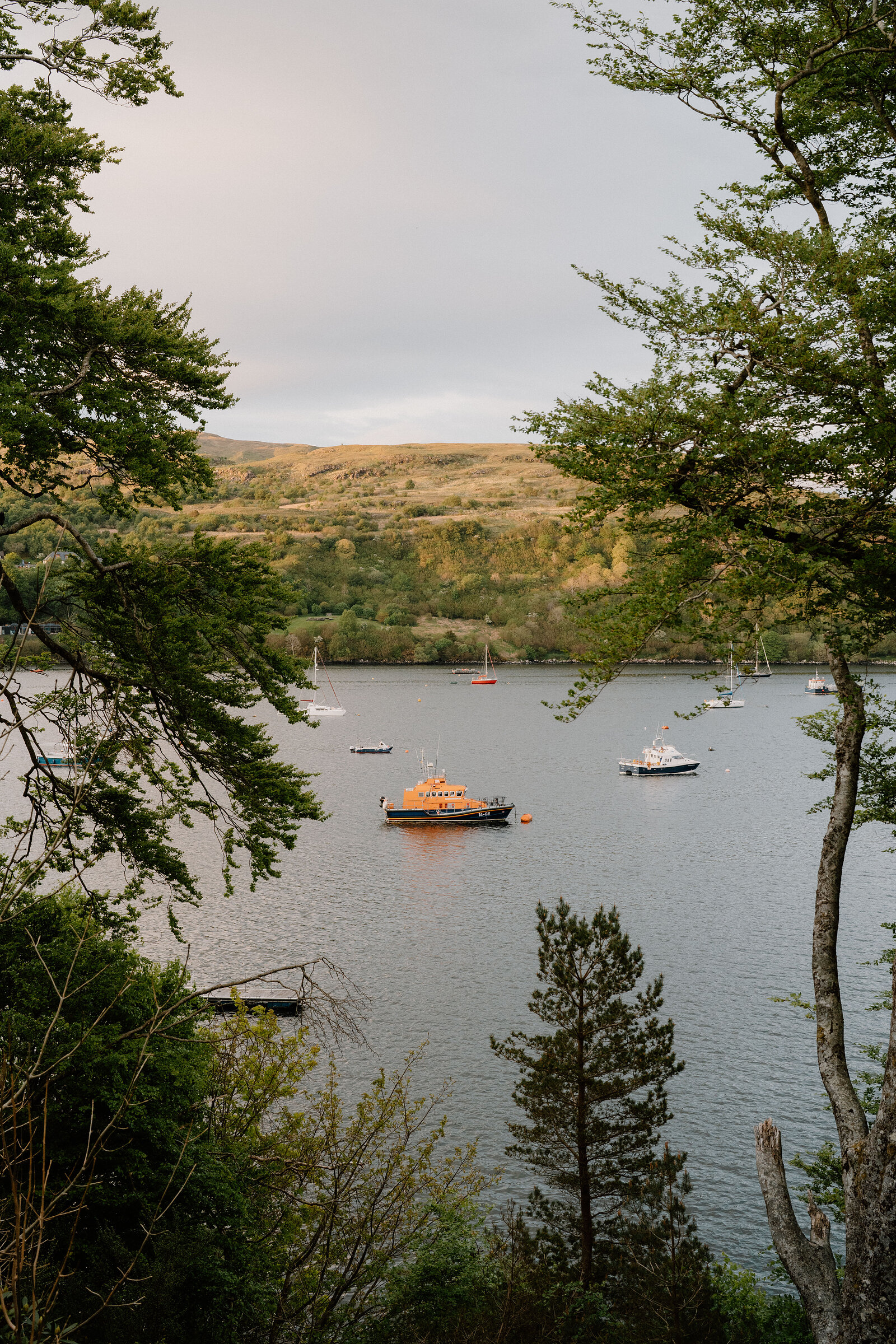 An orange-hulled lifeboat and yachts lie moored in a loch, framed by trees on the Isle of Skye.