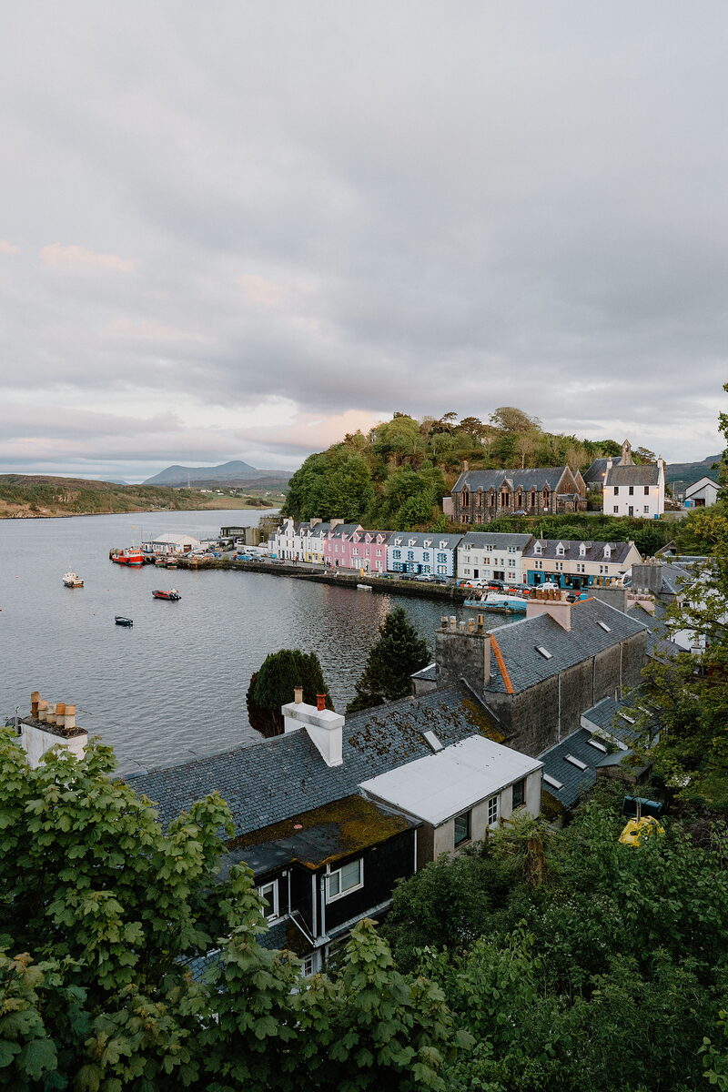 Portree's coloured houses and a church spire rise above a harbour dotted with moored boats.