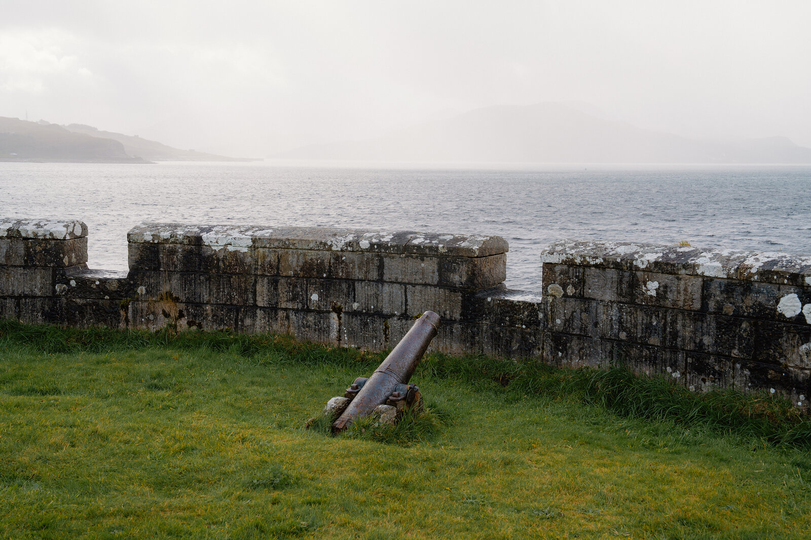 An old cannon points toward the sea from behind a weathered stone parapet.