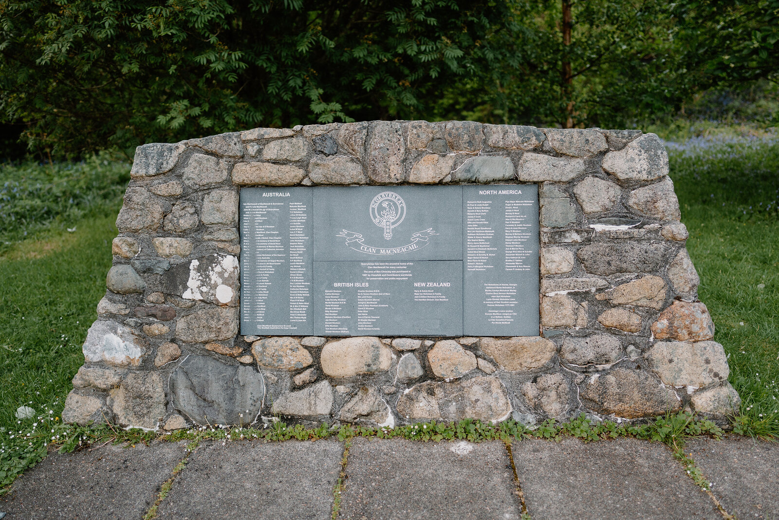 A stone memorial plaque lists names on a low wall in a paved garden.