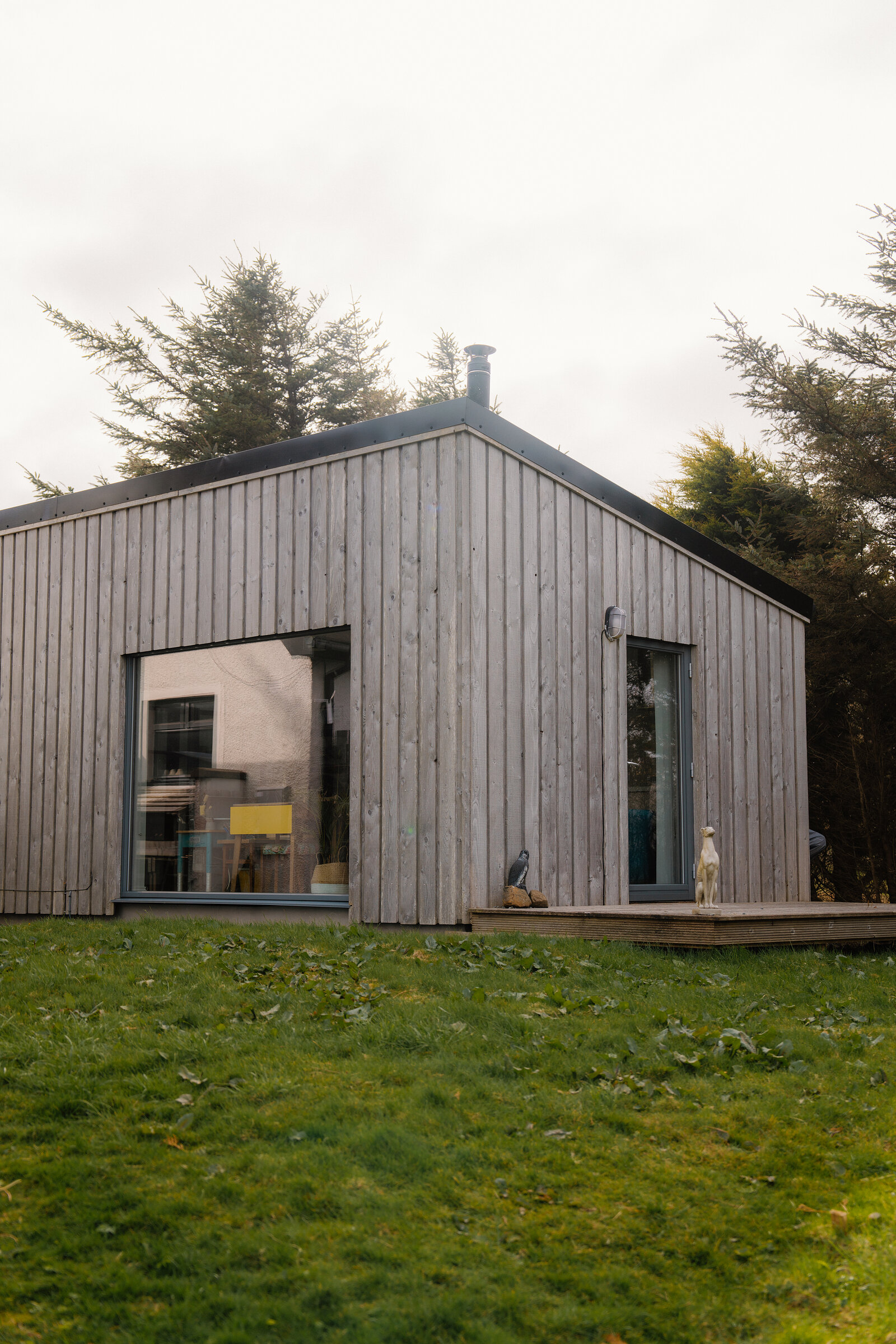 Two birds perch on a deck outside a timber-clad building with large picture windows.