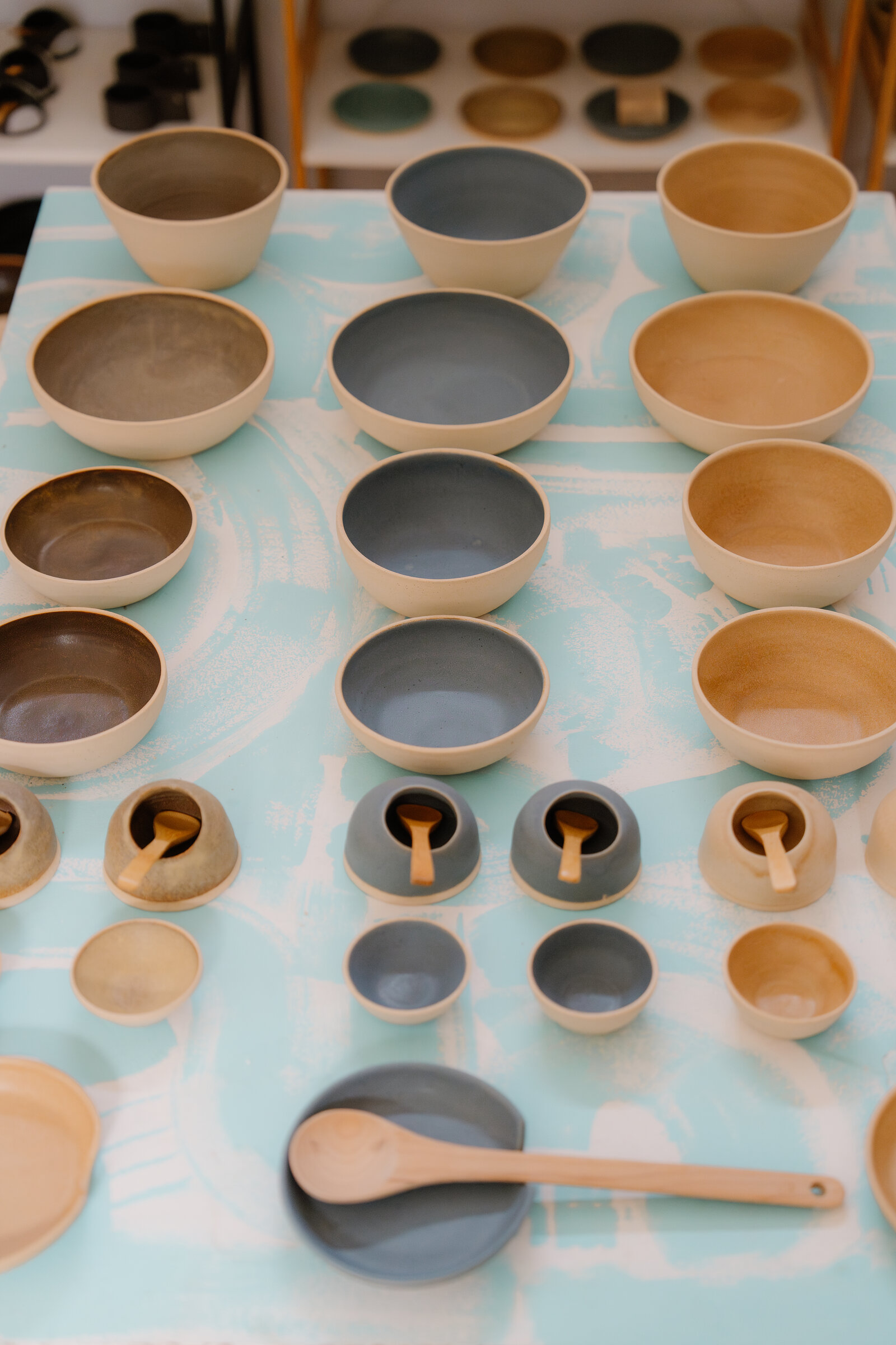 Glazed stoneware bowls in grey, brown and tan sit alongside small lidded pots with wooden spoons.