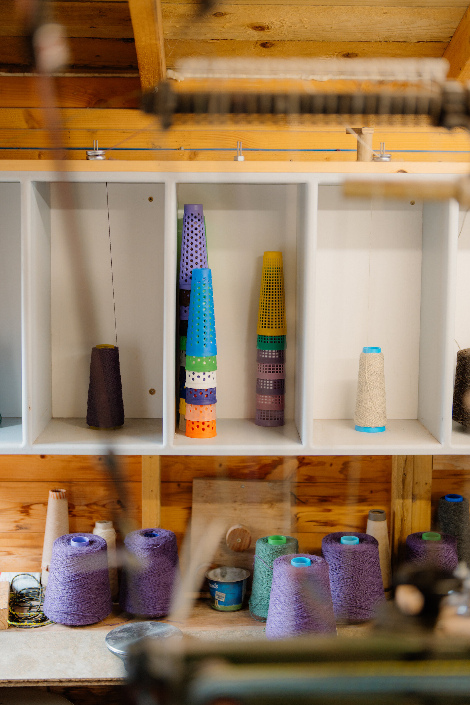 Colourful cones of yarn fill wooden shelving above a workbench in a weaving workshop.