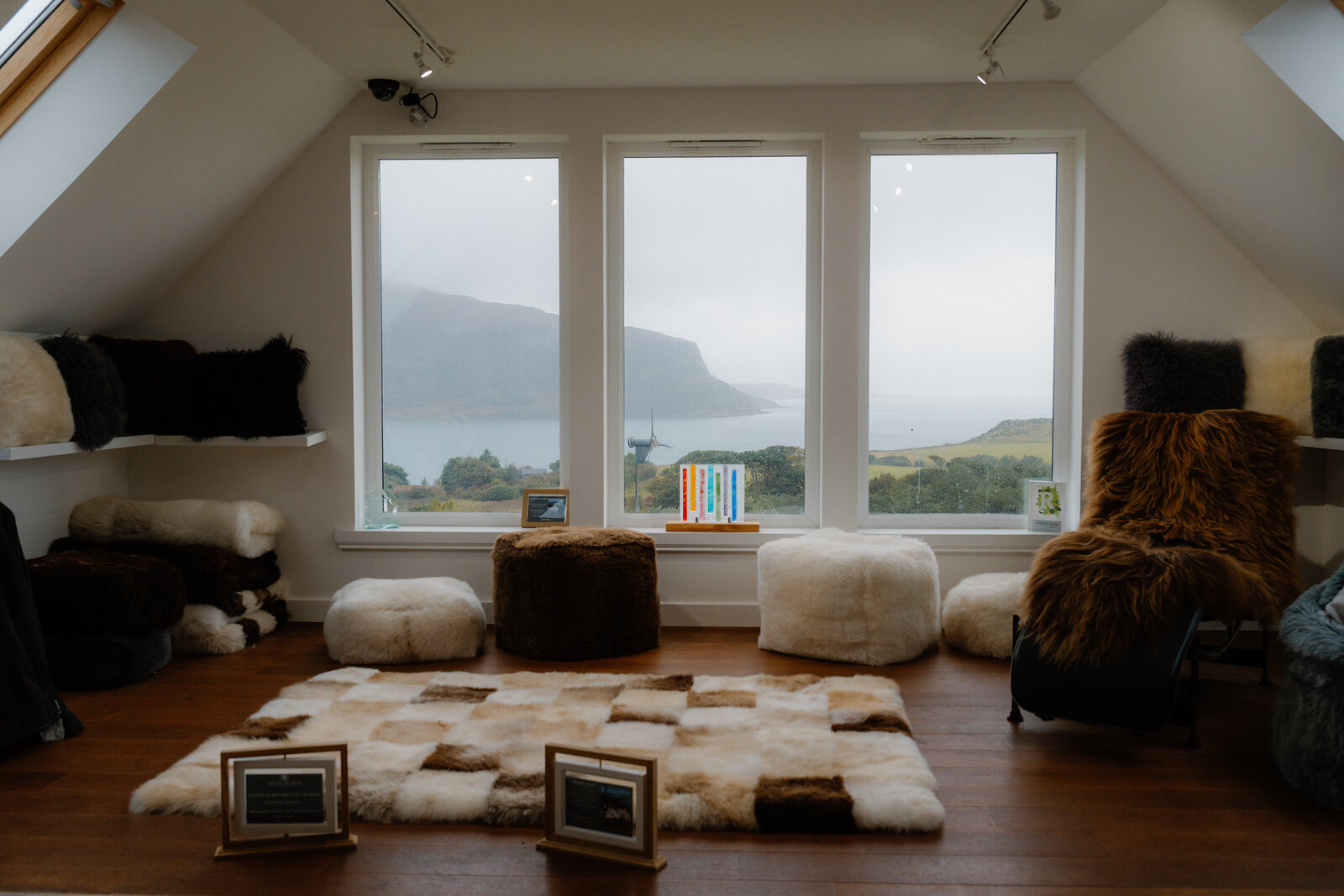 Sheepskin rugs and poufs fill a loft room with panoramic windows overlooking a loch.