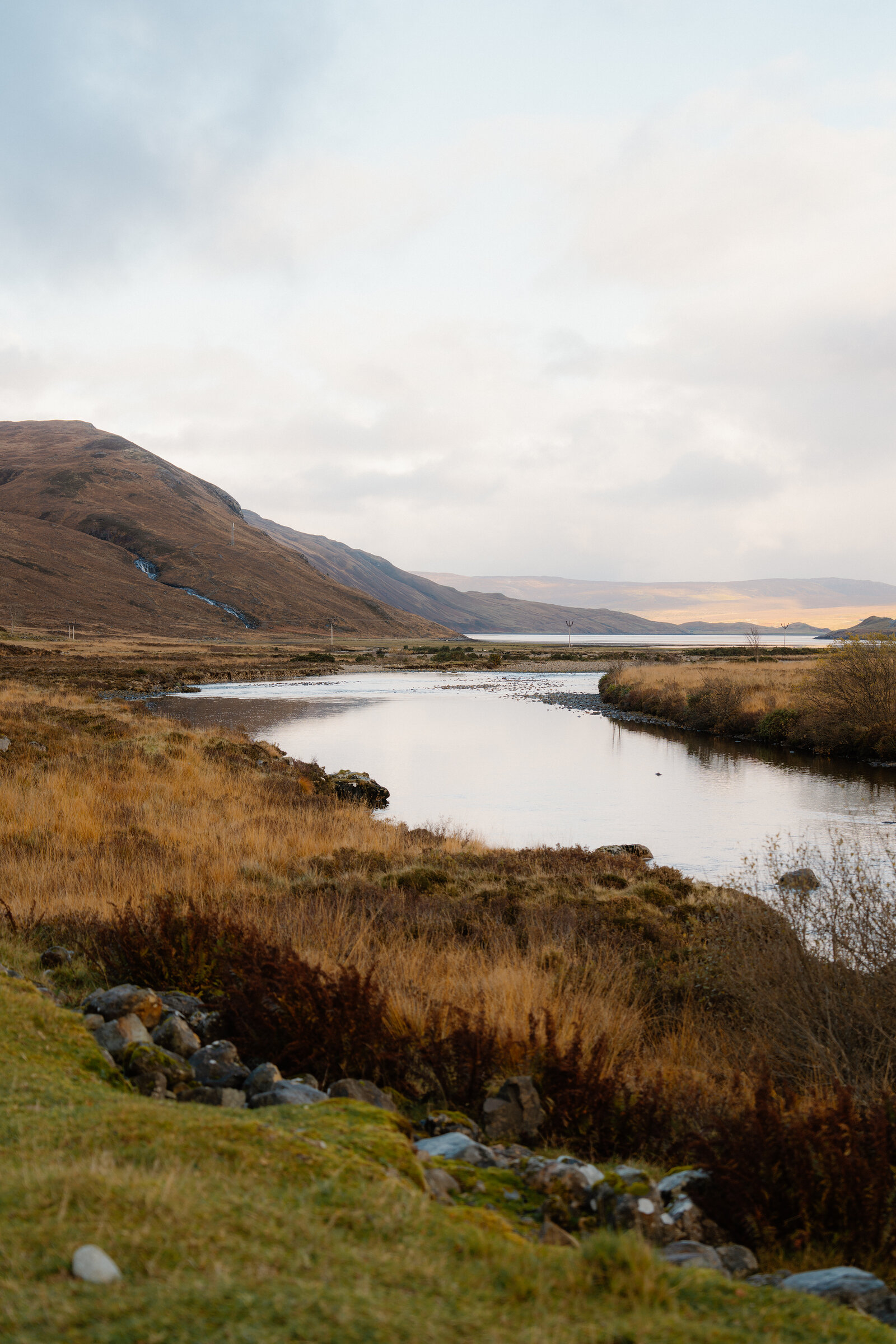 A river winds through moorland toward distant hills beneath a pale sky.