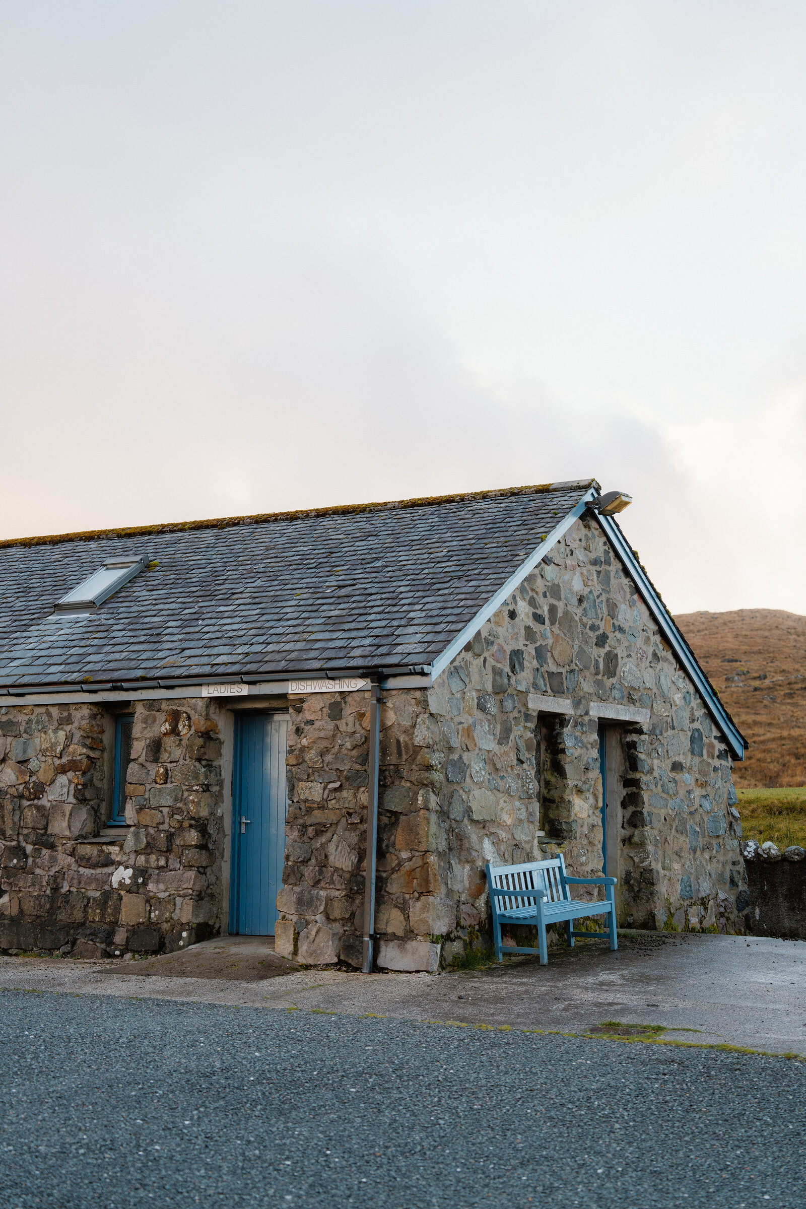 A stone cottage with a pale blue door and matching bench stands beneath a hazy sky.