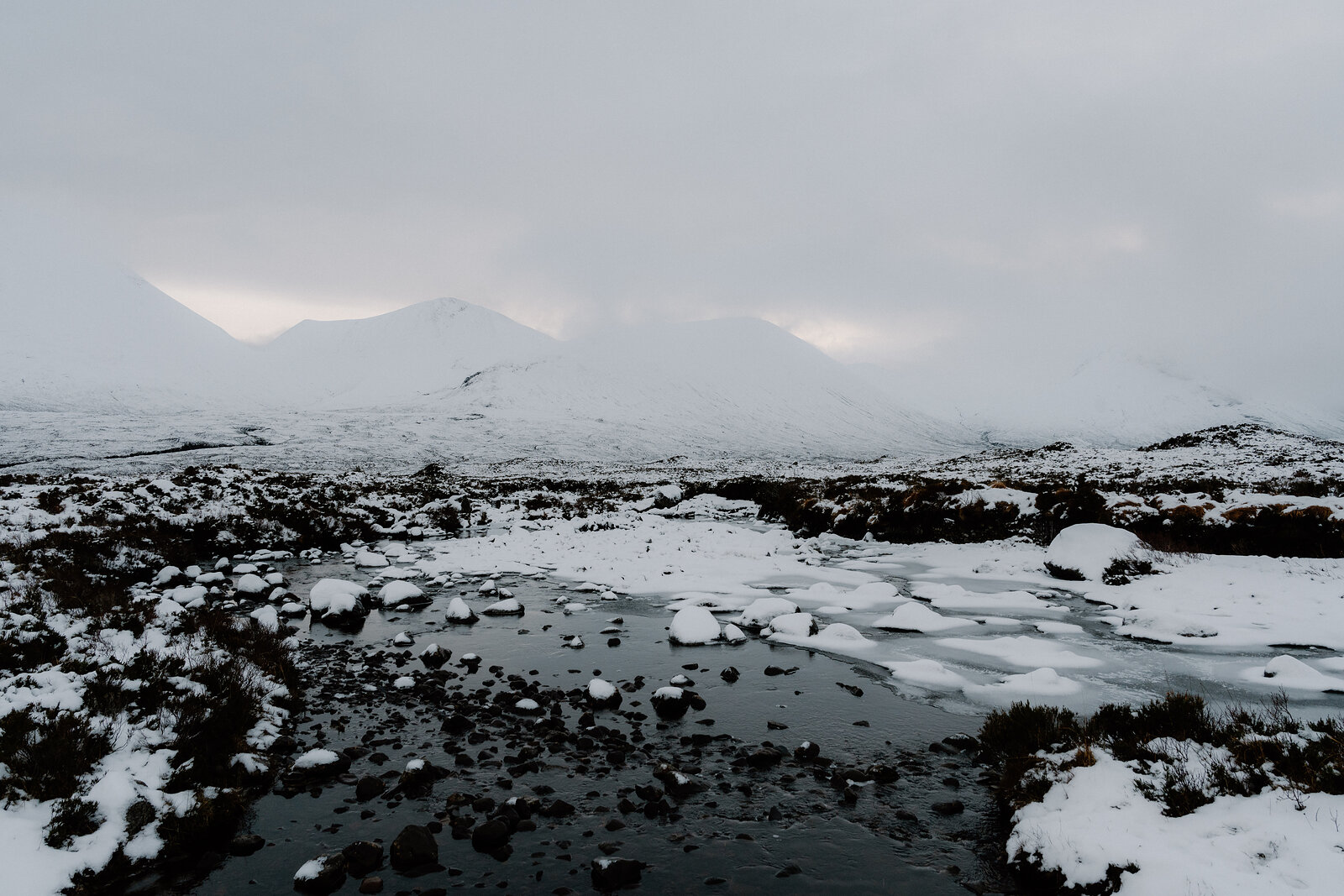 A partly frozen pool sits before snow-covered mountains fading into mist.