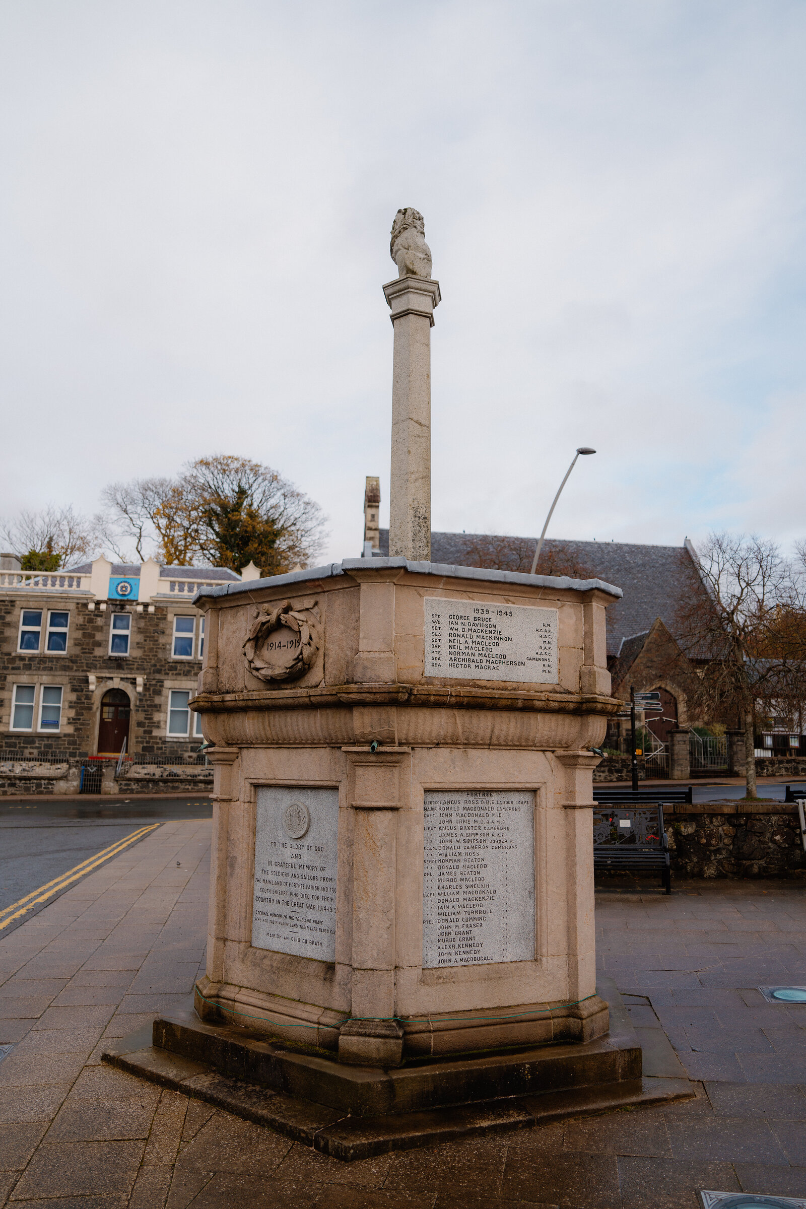 A stone war memorial column topped with a lion tops a plinth on a town square.