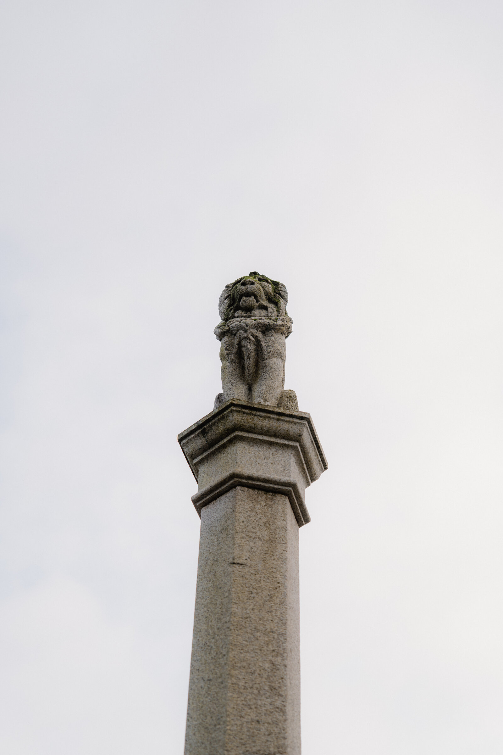 A carved lion sits atop a stone war memorial column against a pale sky.
