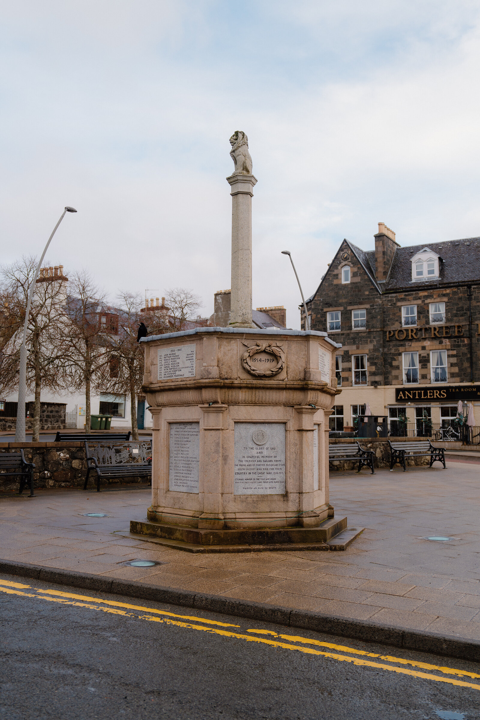 The Portree war memorial column stands on a paved square before the 'Antlers' pub.