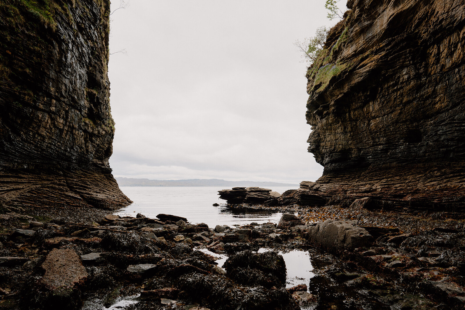 The narrow rock gorge opens toward calm water in the distance, its stony floor leading down to the shore.