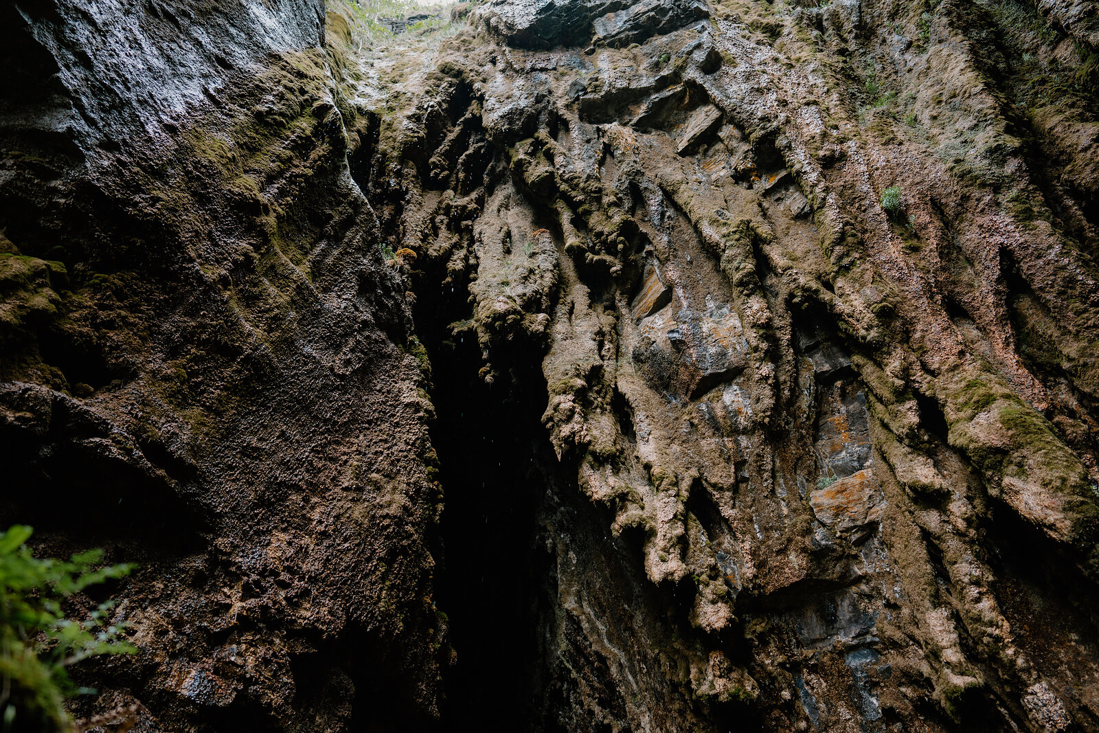 Weathered orange-brown rock strata rise inside the gorge, with a dark recess at the base and moss growing to one side.