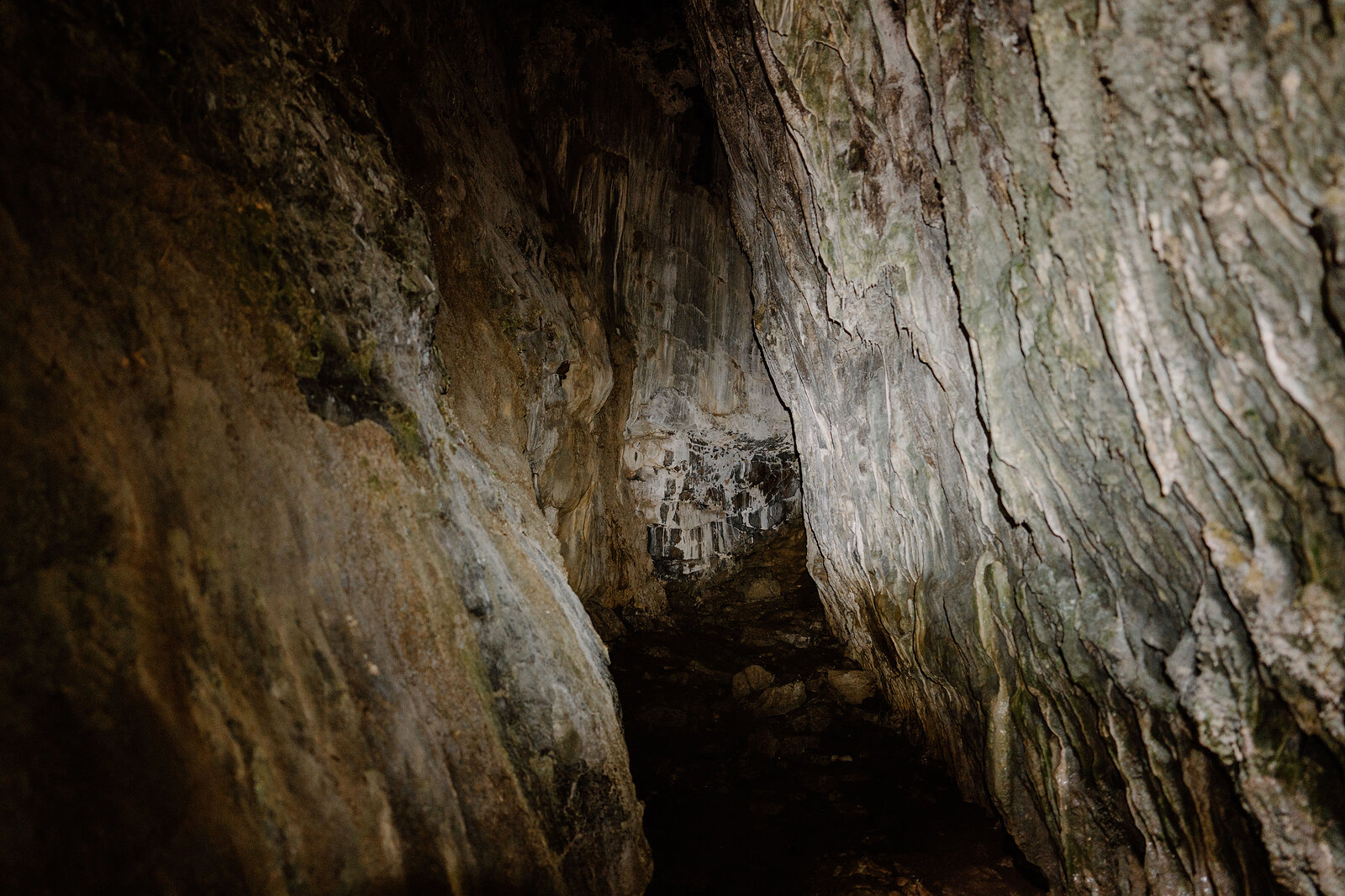 Pale rippled rock walls line a cave passage, with a shaft of light picking out the way ahead.