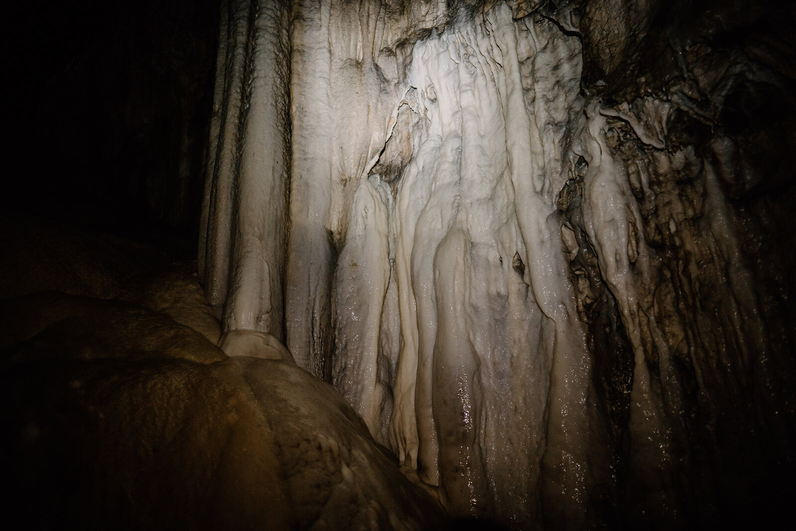 Pale, ribbed calcite flowstone drapes the cave wall, catching torchlight against the dark rock around it.