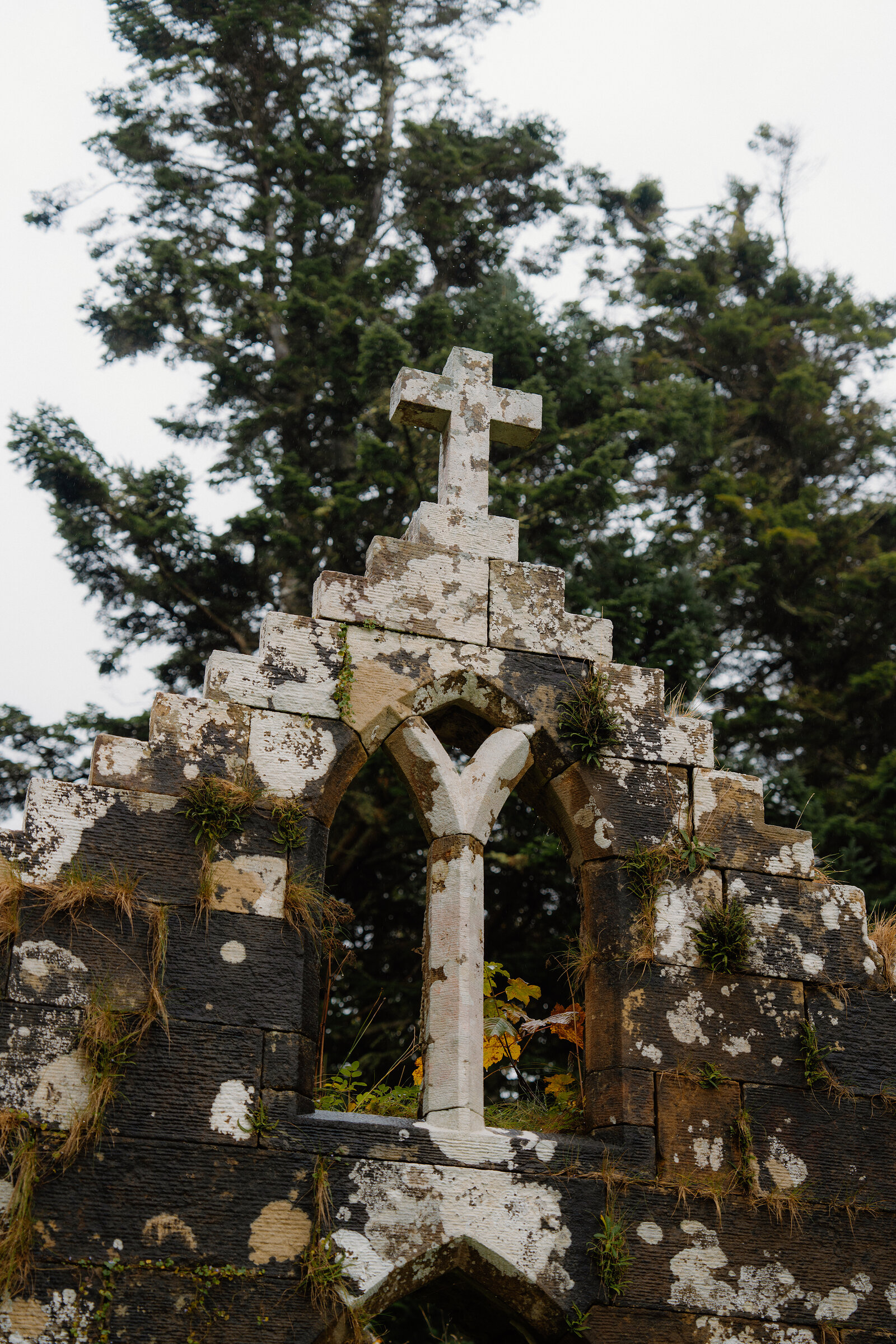 A stone cross on the stepped gable of the MacLeods' burial vault beside St Moluag's Chapel, framed by conifers.