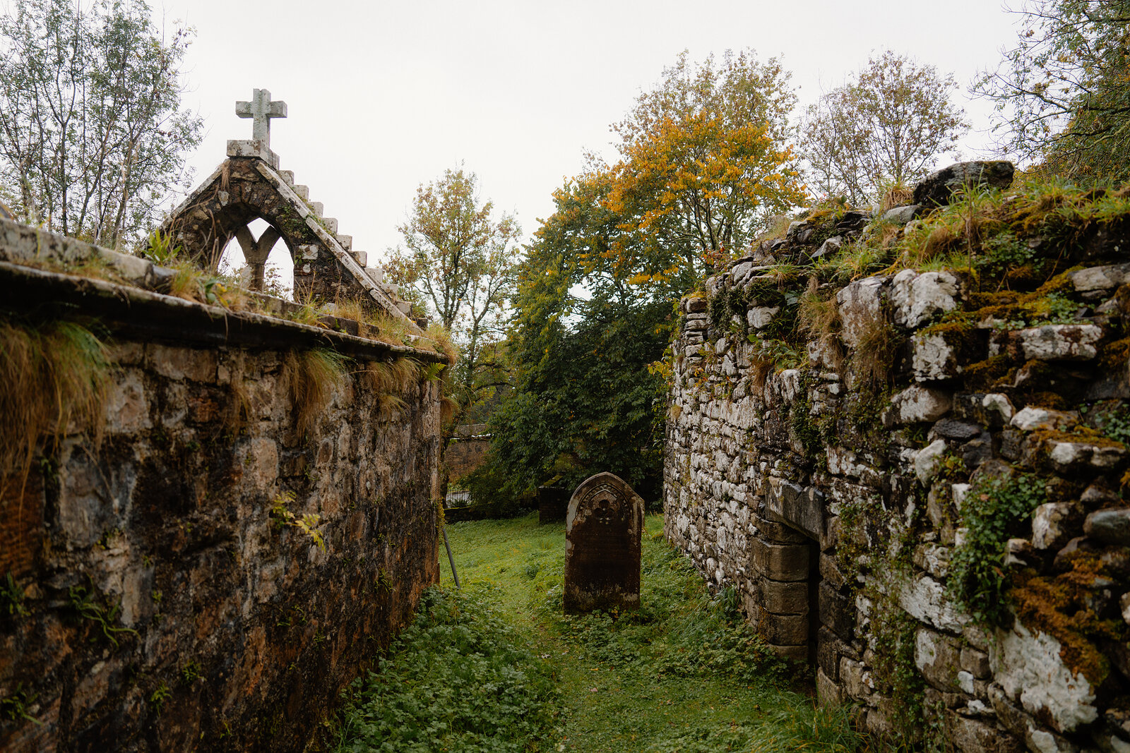 The pointed window and cross of the MacLeod vault at St Moluag's, a gravestone in the grass by the chapel wall.