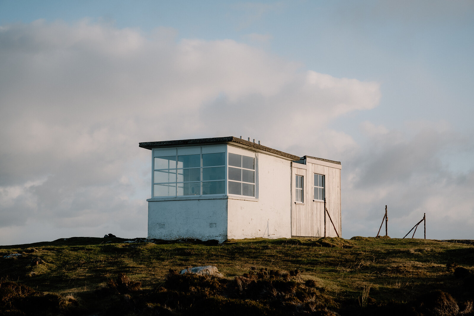 A white single-storey lookout building with a bank of windows sits alone on a grassy clifftop.