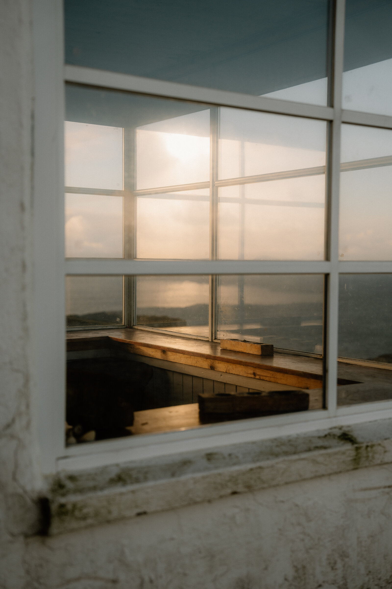 A wooden window ledge inside The Lookout catches the sunset glow over the sea beyond.