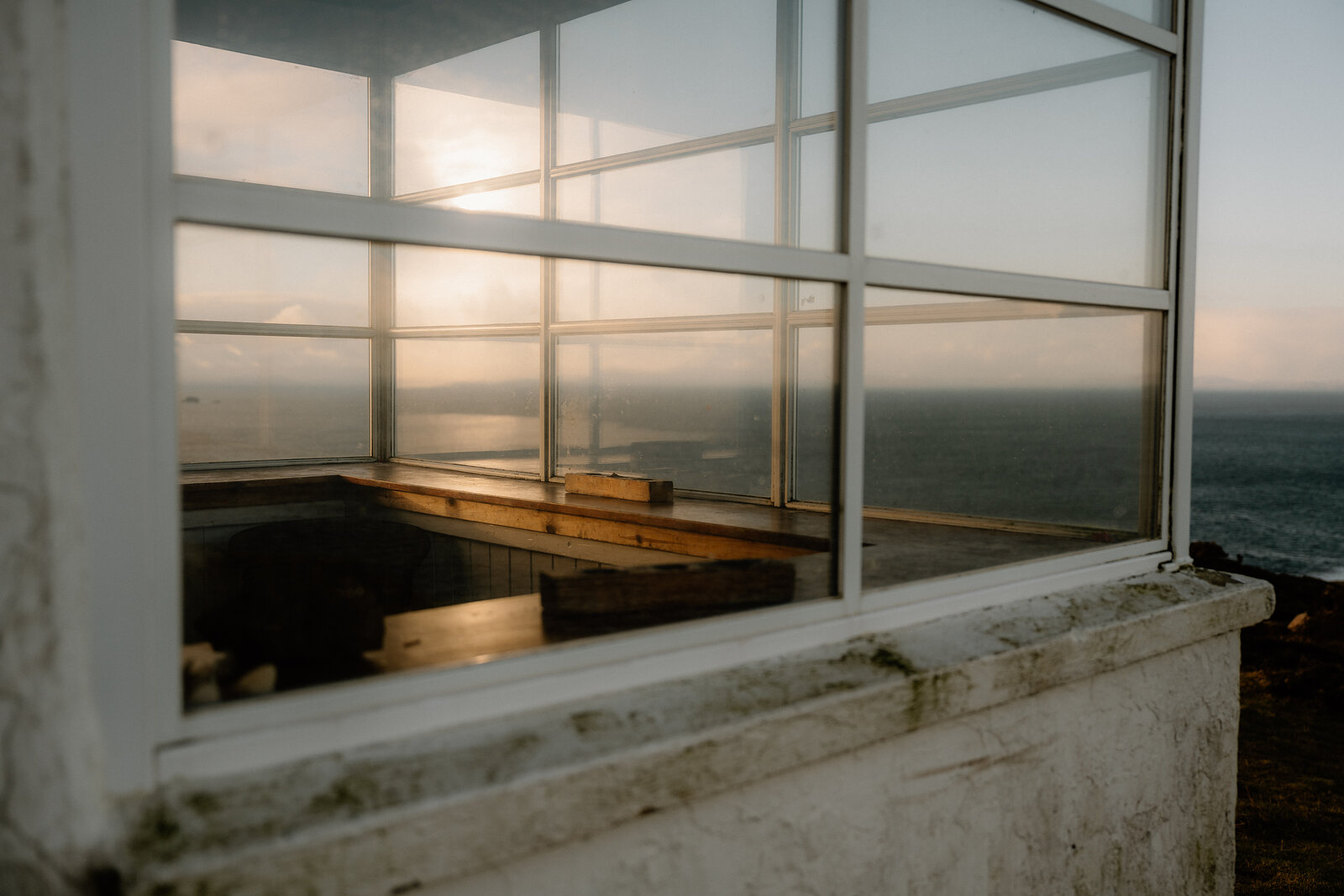 The sun sets over the sea, framed through The Lookout's corner windows and wooden ledge.
