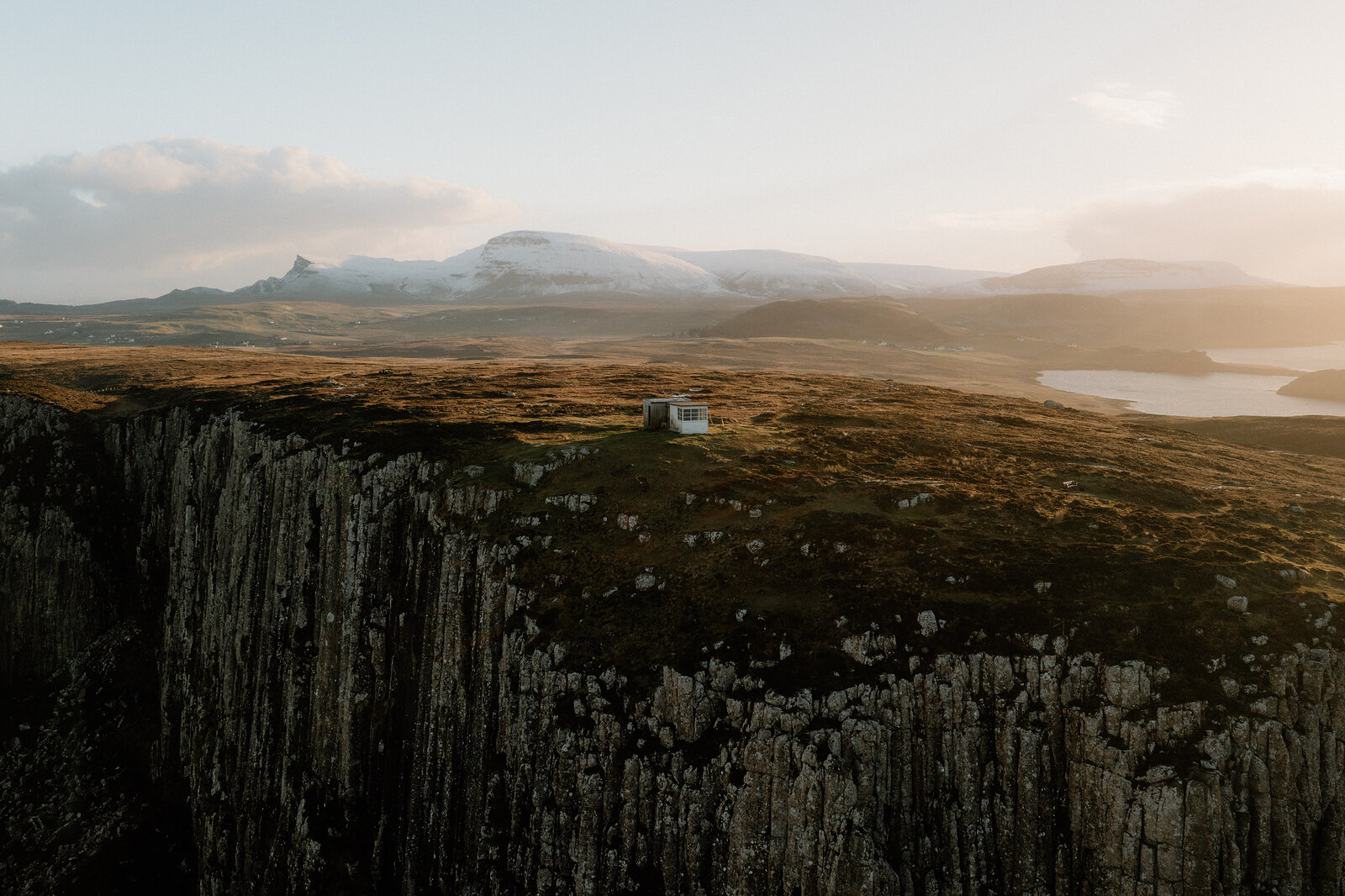 The Lookout sits alone on a clifftop above sheer columnar rock, a loch and snow-capped peaks visible in the distance.