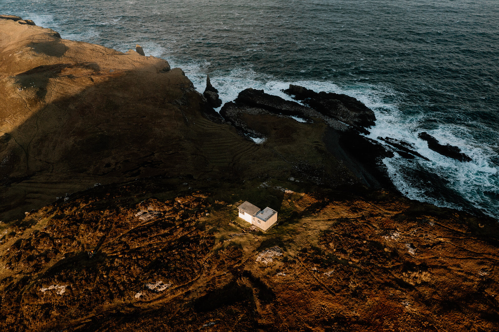 The Lookout sits at the tip of a narrow headland surrounded by dark rocky coves and crashing waves.