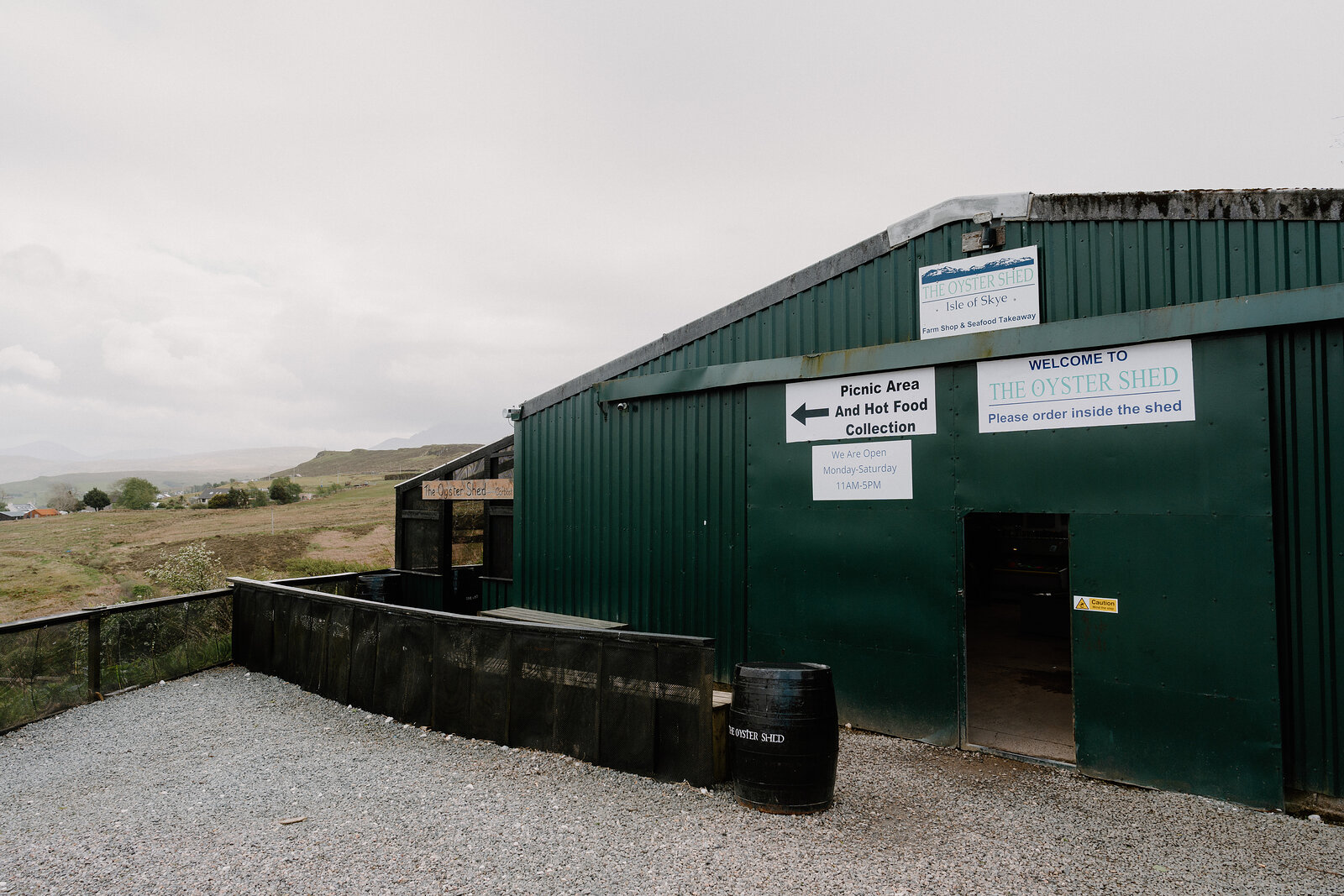 The Oyster Shed's green corrugated building has a covered porch signed Welcome, with instructions to please order inside.