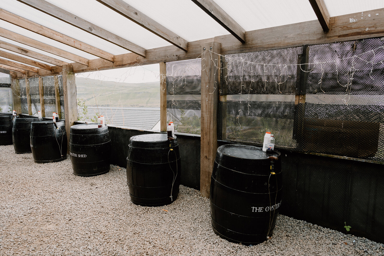 Black barrels lettered with the shed's name line a covered seating area with mesh screens overlooking the moorland.