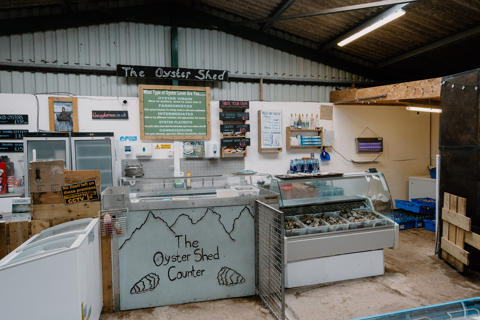 The Oyster Shed's counter is set beneath a chalkboard sign, a glass display case of oysters beside a hand-painted mural.