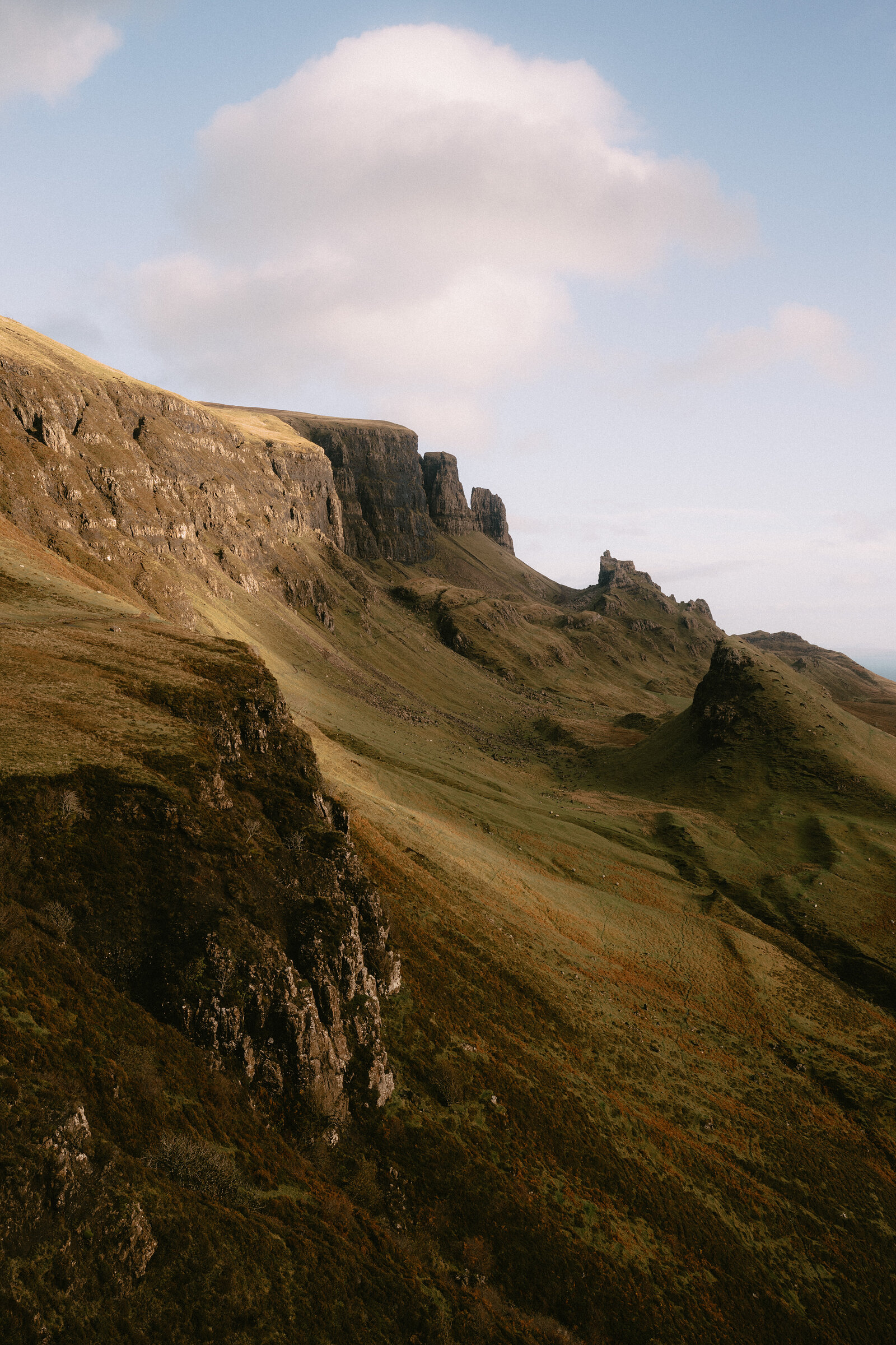 Jagged rock pinnacles rise from the Quiraing's grassy slopes beneath a partly clouded sky.