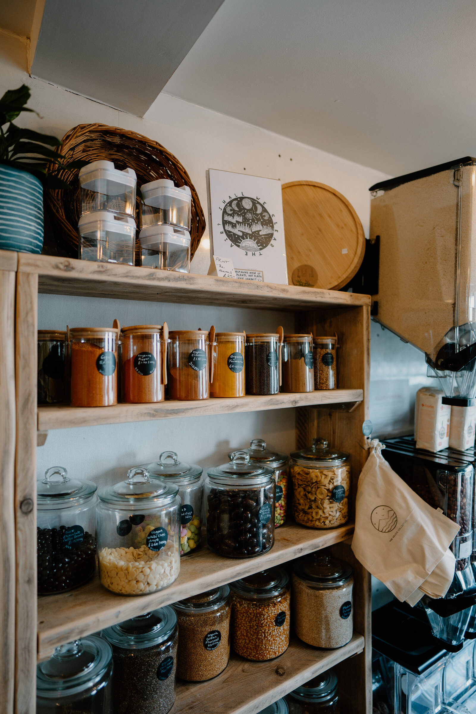 Glass jars of dried beans and grains sit on wooden shelves beside refill bottles and a moon-themed print.