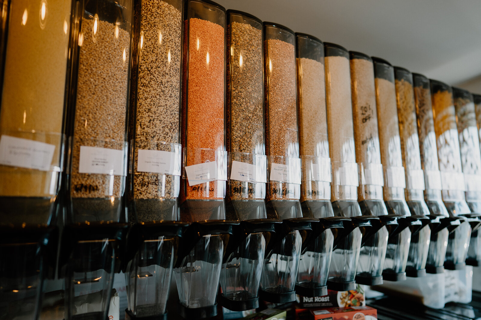 A row of bulk-food dispensers filled with colourful grains and pulses lines a shop counter.