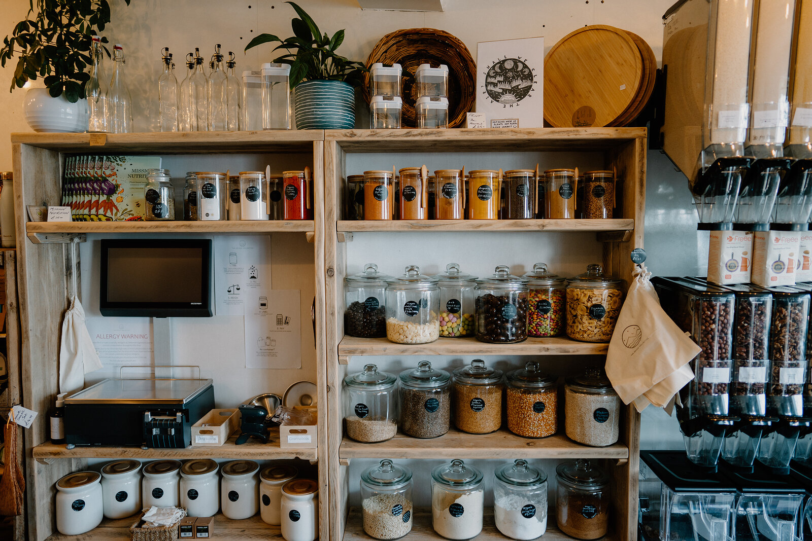 Labelled jars of coffee, tea and dried goods fill wooden shelving beside a set of weighing scales.