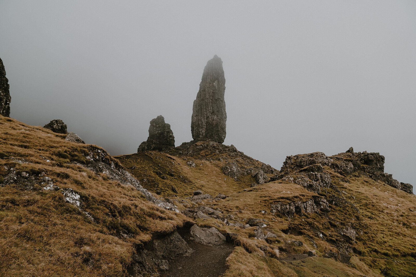 The Old Man of Storr's spire rises above a worn path through the misty hillside.