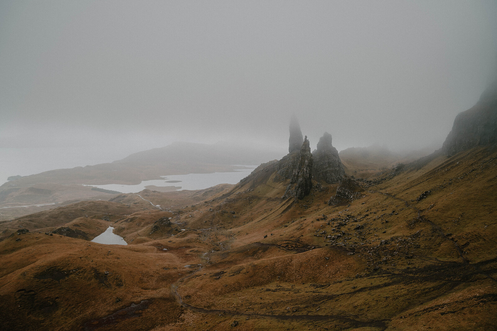 The Old Man of Storr's rock spires rise above a misty valley, a loch visible in the distance below.